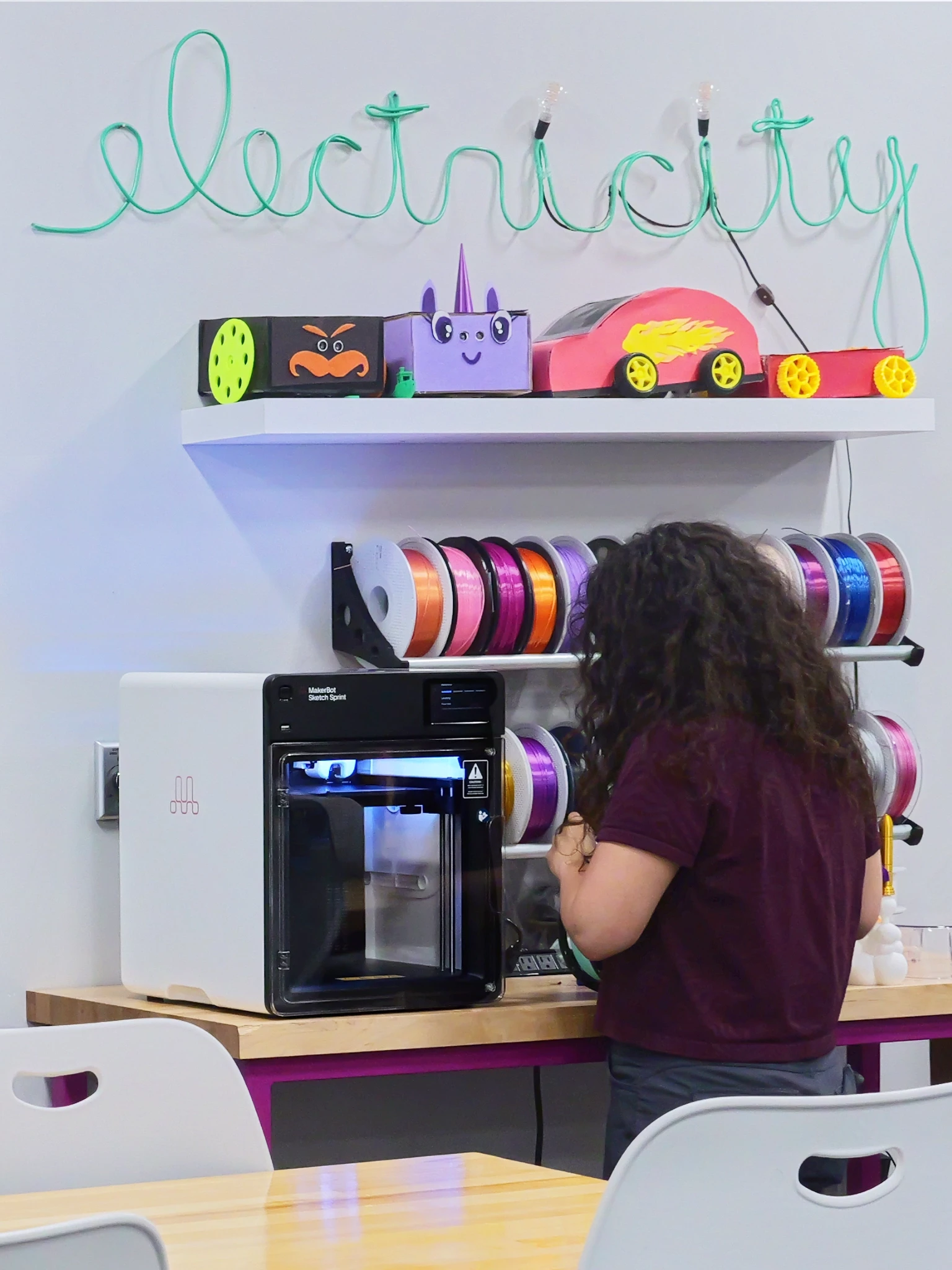 Modern home office setup with a monitor, ergonomic chair, keyboard, and indoor plants near a window with blinds.