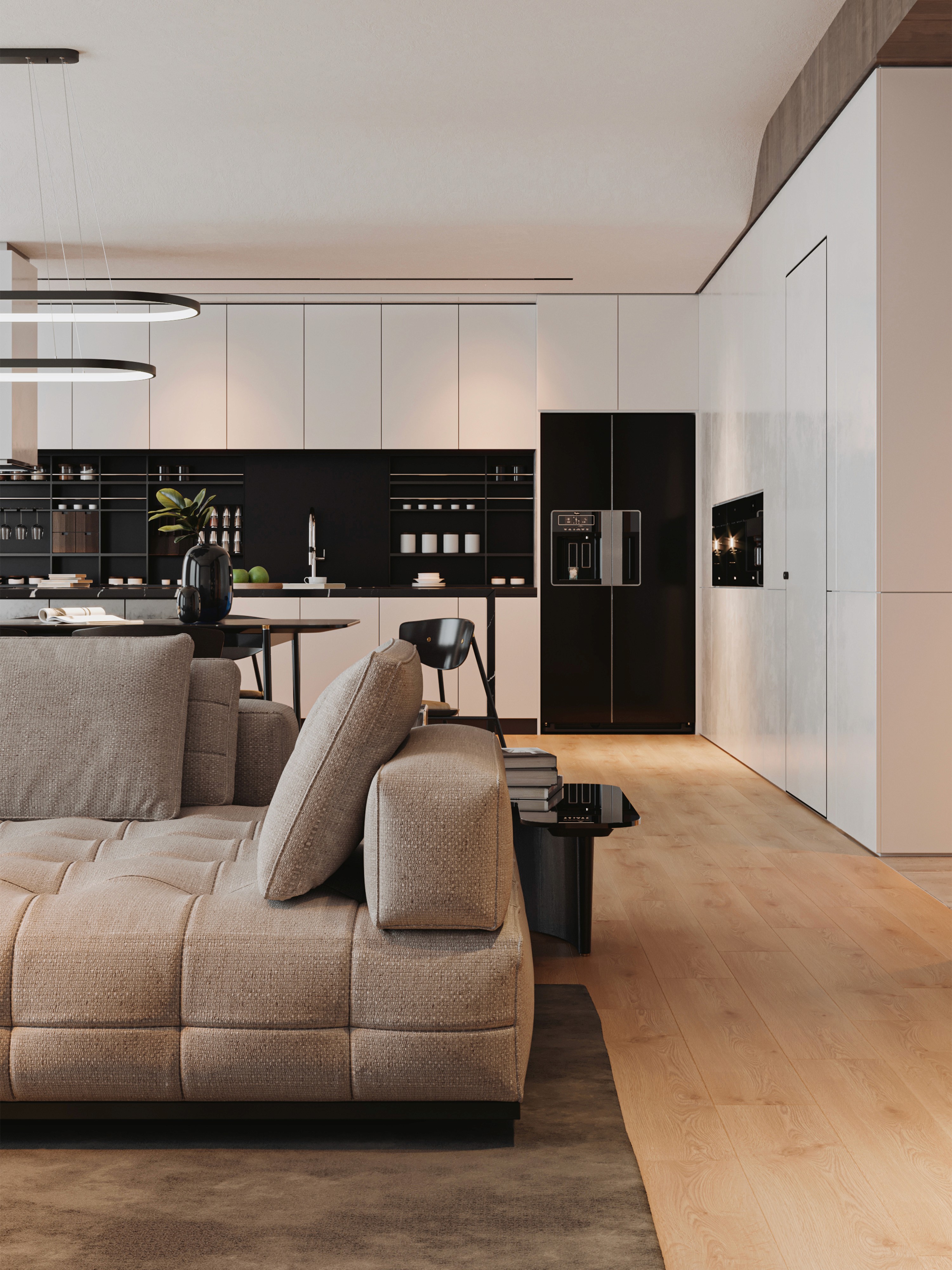 Render architettonico fotorealistico di un moderno open space con cucina a vista. In primo piano un divano modulare beige su tappeto scuro; sullo sfondo cucina minimalista bianca con backsplash nero, elettrodomestici moderni e pavimento in parquet chiaro.