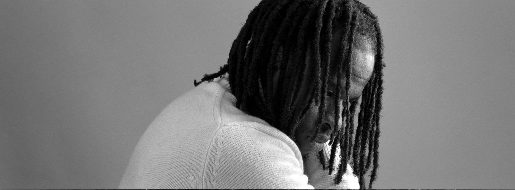Film photography with flash: A man slightly rotated away from the point of view, his hair slightly obscuring his face using Hasselblad XPan, wearing a white sweater with locks, close-up panoramic portrait of model in thought, black and white Ilford Delta.