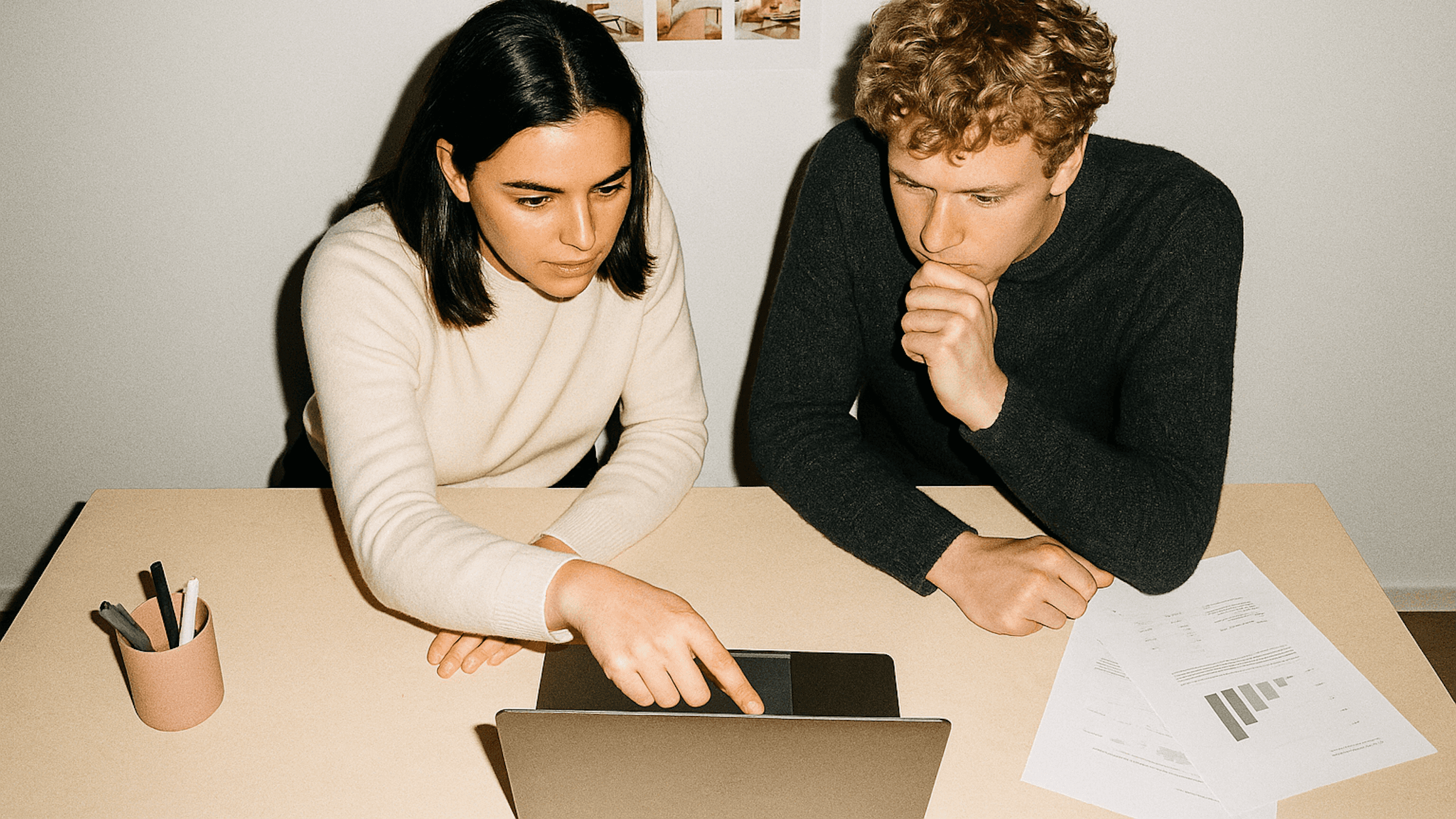 Two people collaborating at a desk, reviewing data on a laptop with charts and notes, in a modern and minimal workspace.