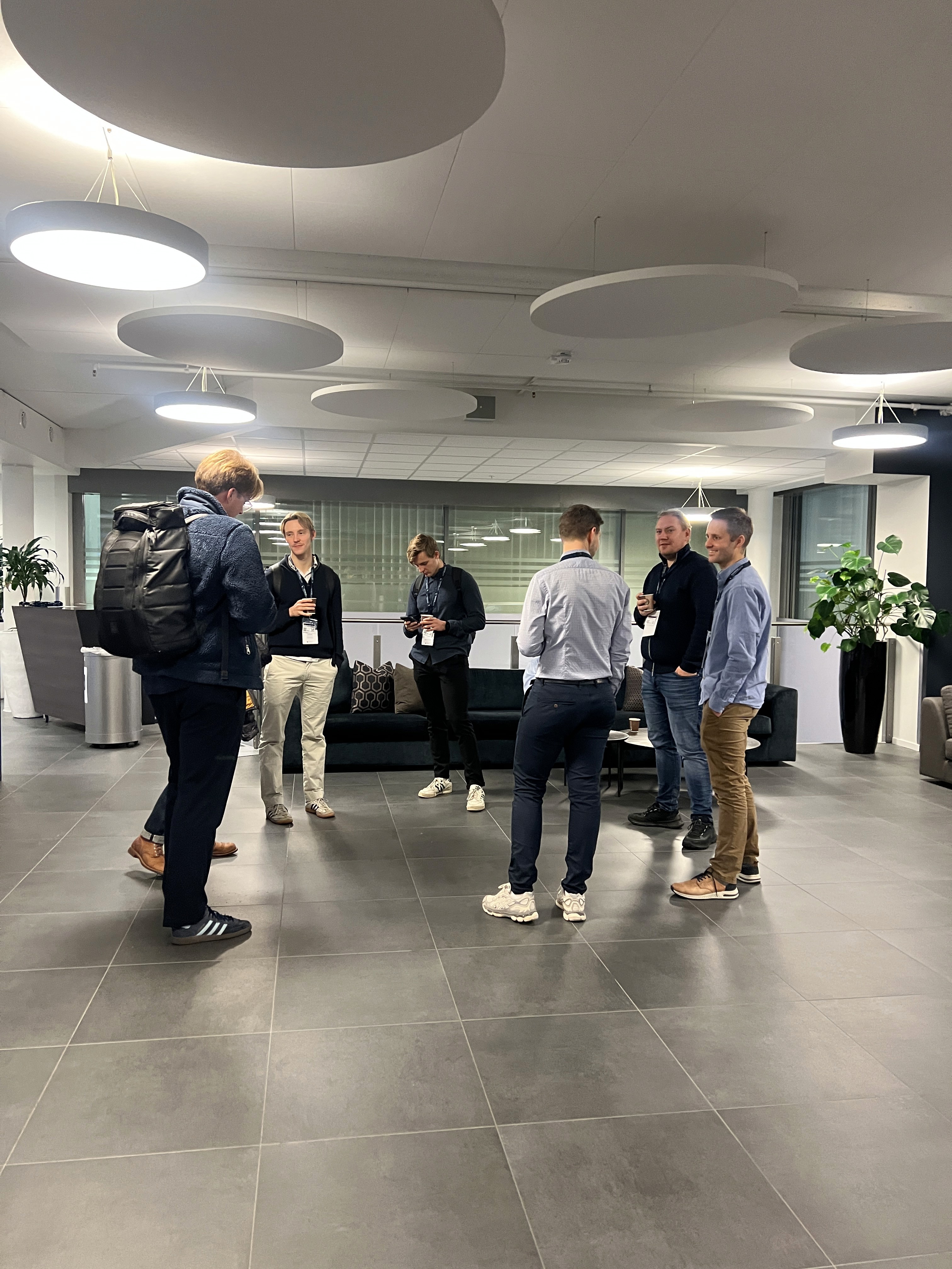 A group of people engaged in conversation in a modern office lobby with plants and contemporary decor.