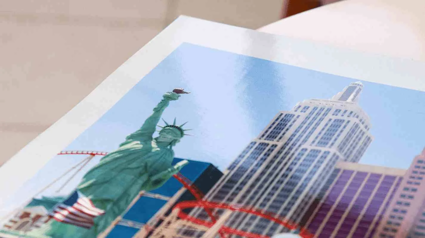 Close de página de fotolivro com impressão brilhante, exibindo a Estátua da Liberdade e arranha-céus ao fundo