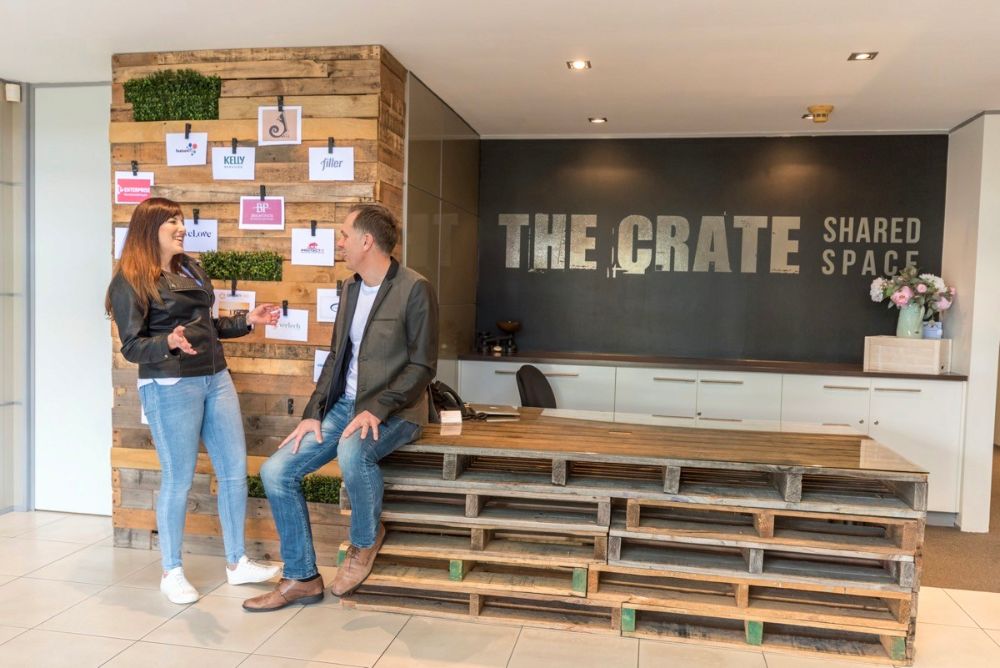 A man and a woman, one sitting, talking to each other at The Crate Hamilton.