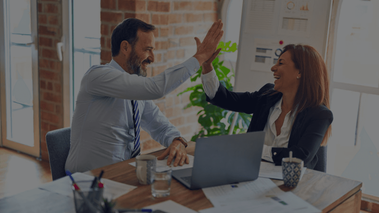 Fotografía de un asesor bancario y un cliente sonriendo mientras estrechan la mano frente a una computadora, representando el éxito en una gestión de consolidación de deuda.