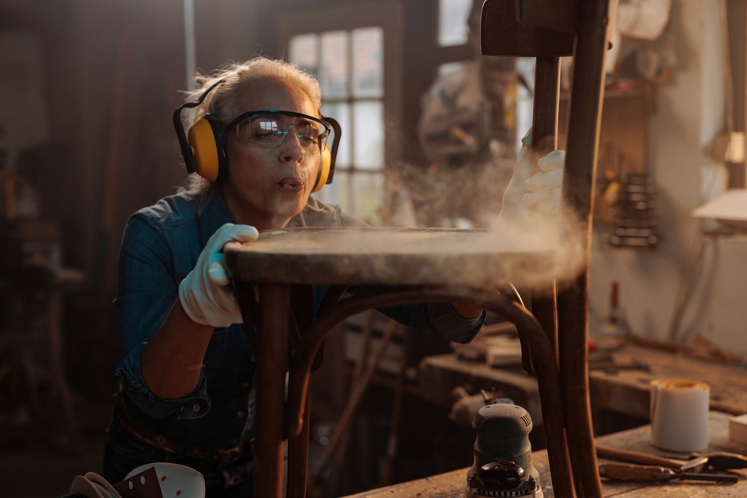 Photo of carpenter blowing dust from furniture. 
