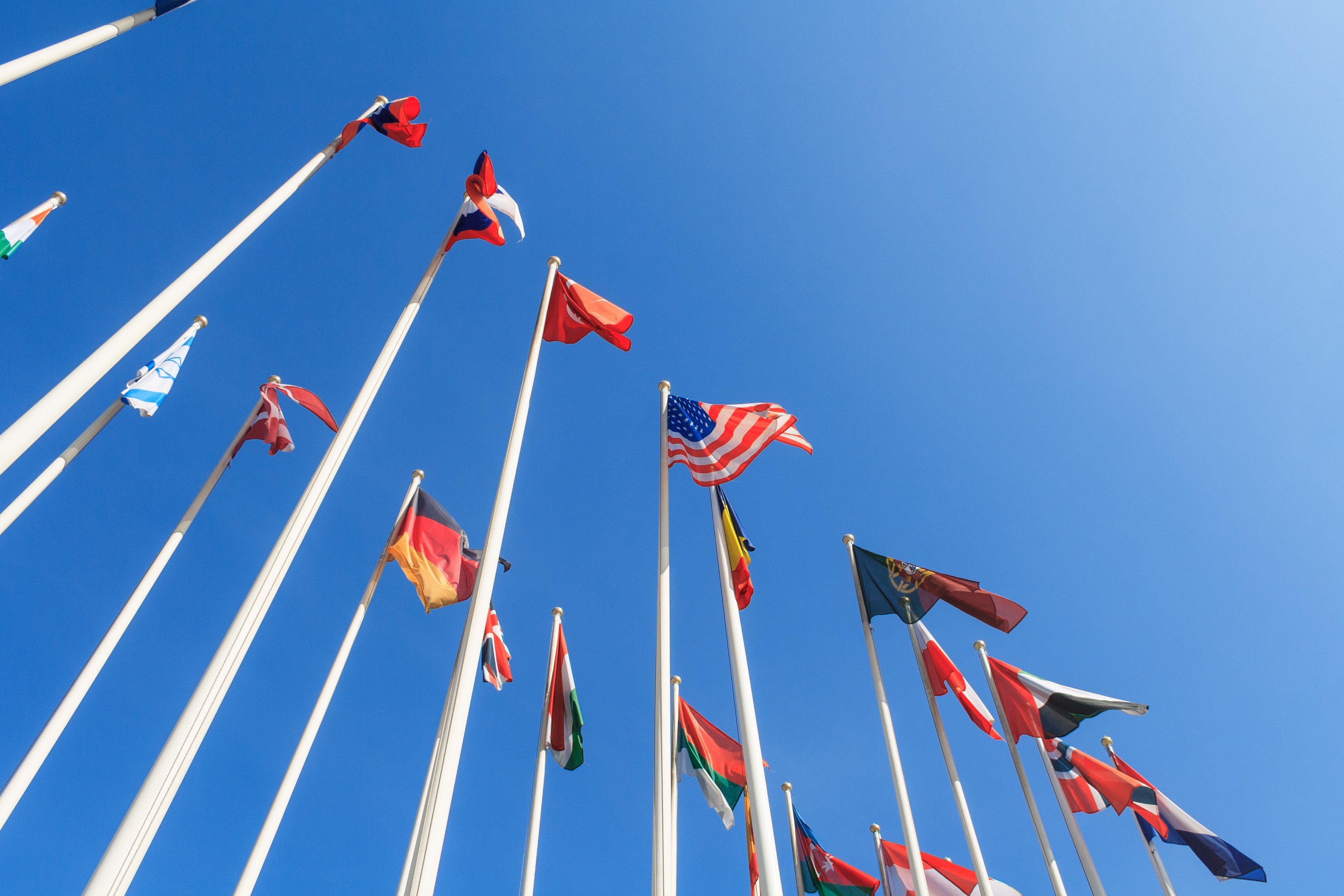 Bottom view of a rows of flags of different countries of the world, flutters in the wind, against a clear blue sky.