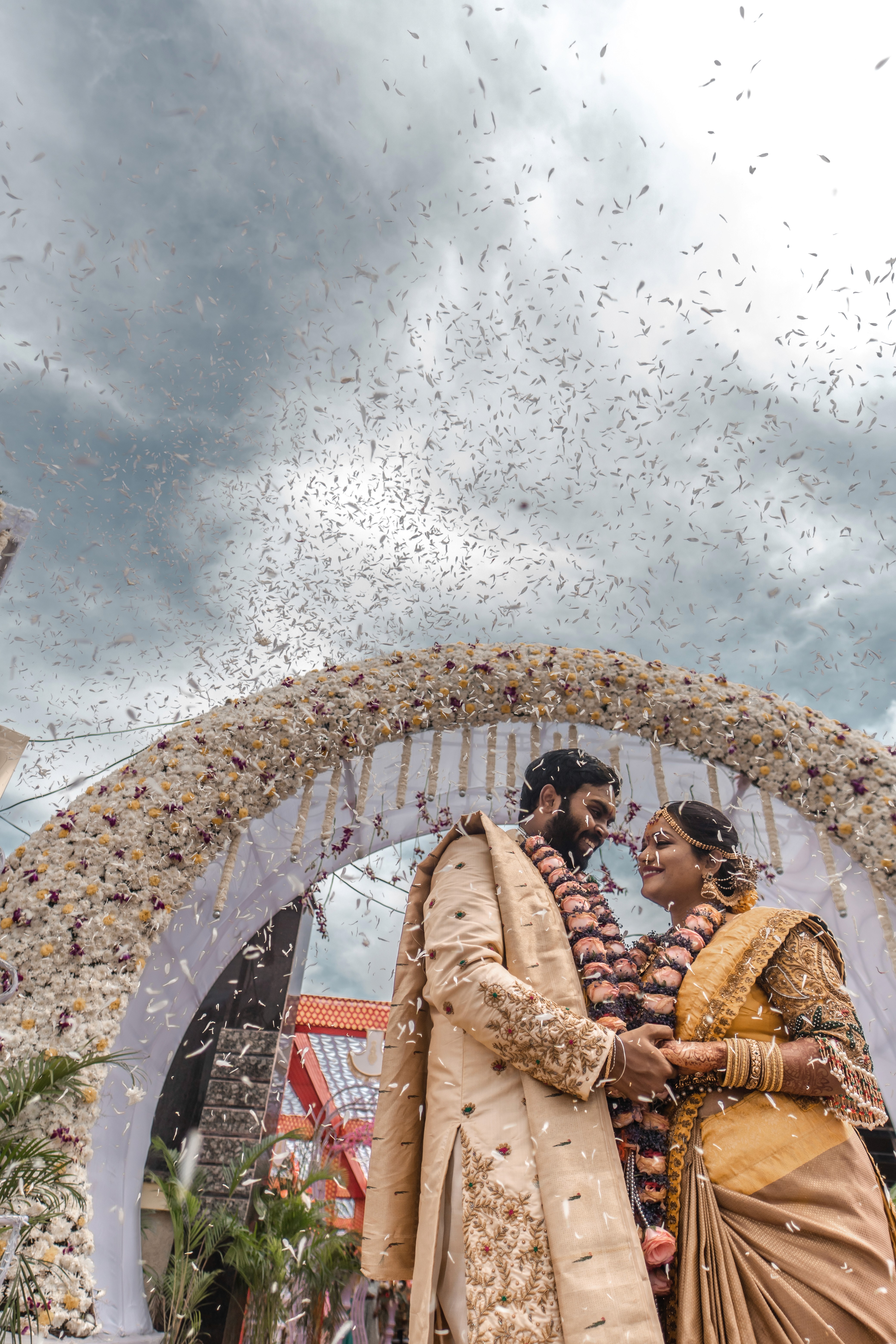 Samsrita and Ramkumar smile as flowers rain down during their wedding. Captured by Out of The Blues Fine Art Wedding Photography in Hyderabad.