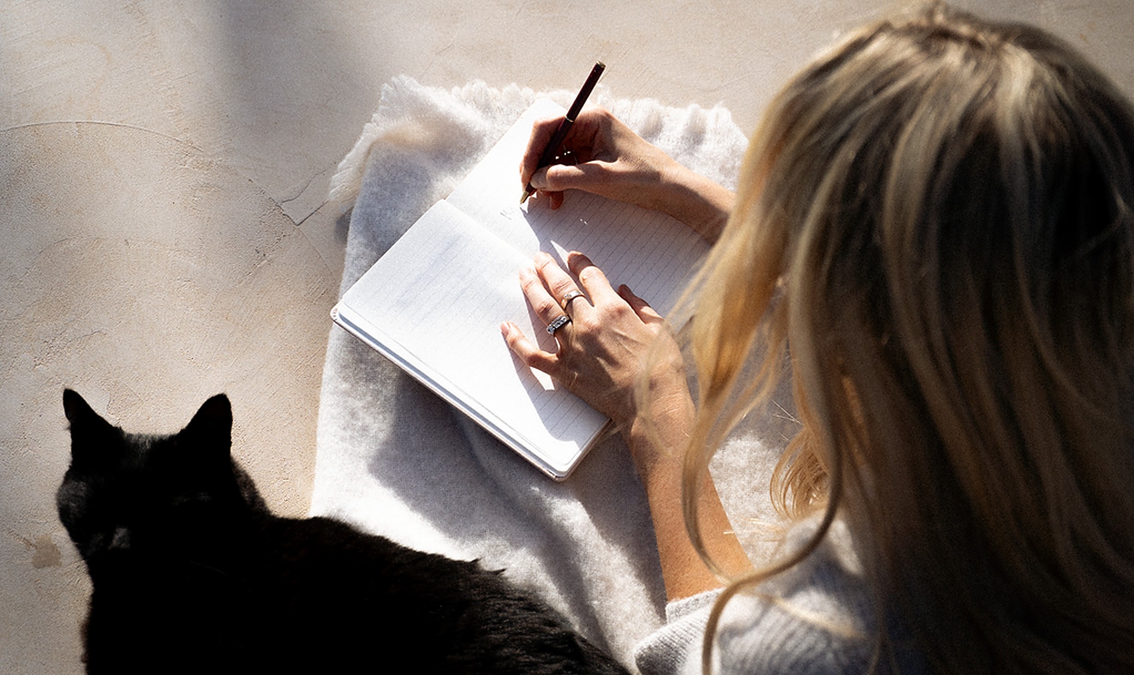 Woman journaling beside a black cat in soft light, exploring self-knowledge and how sex drive changes with age