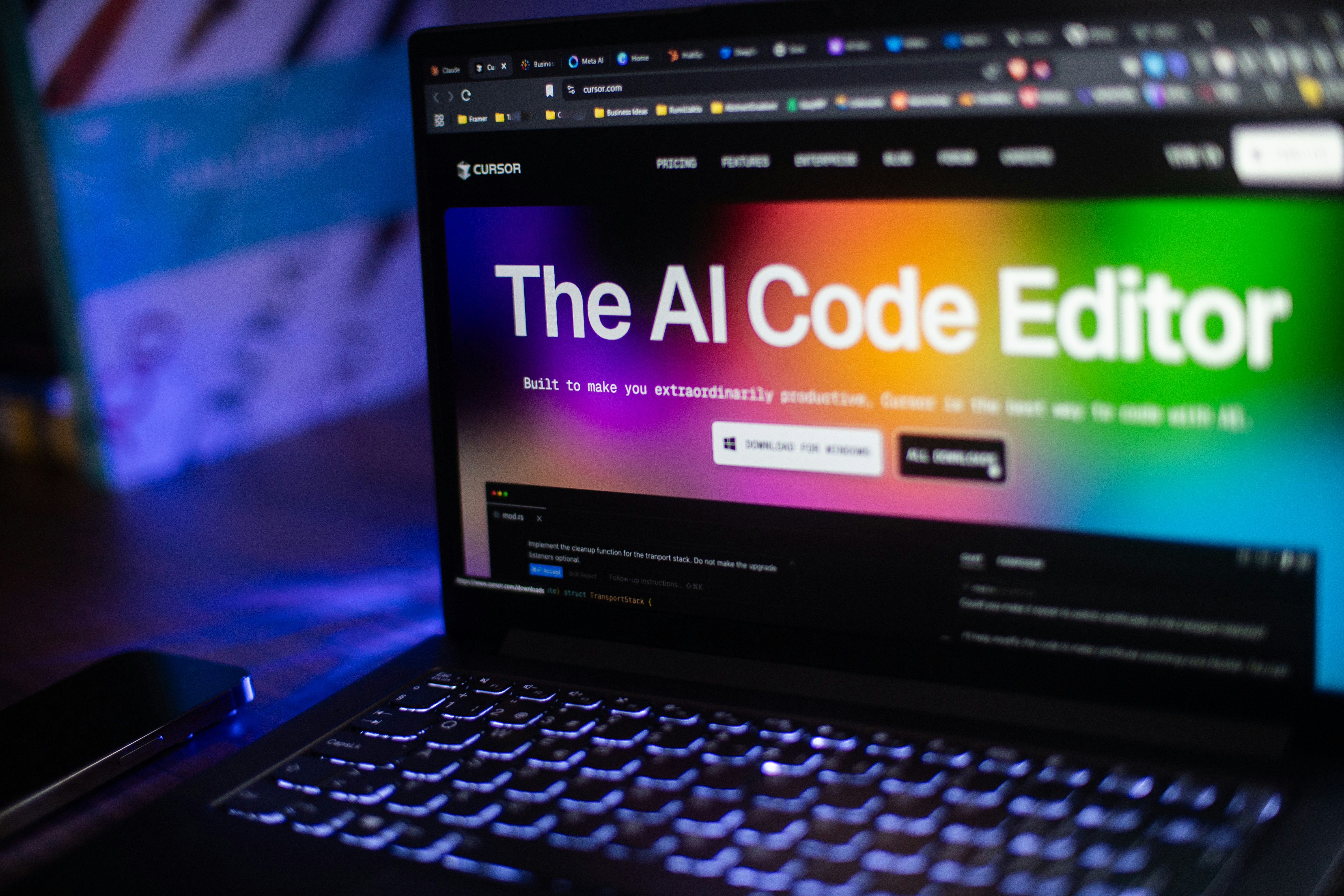 Laptop screen showing the Cursor website with “The AI Code Editor” headline, photographed in low light with colorful blurred background