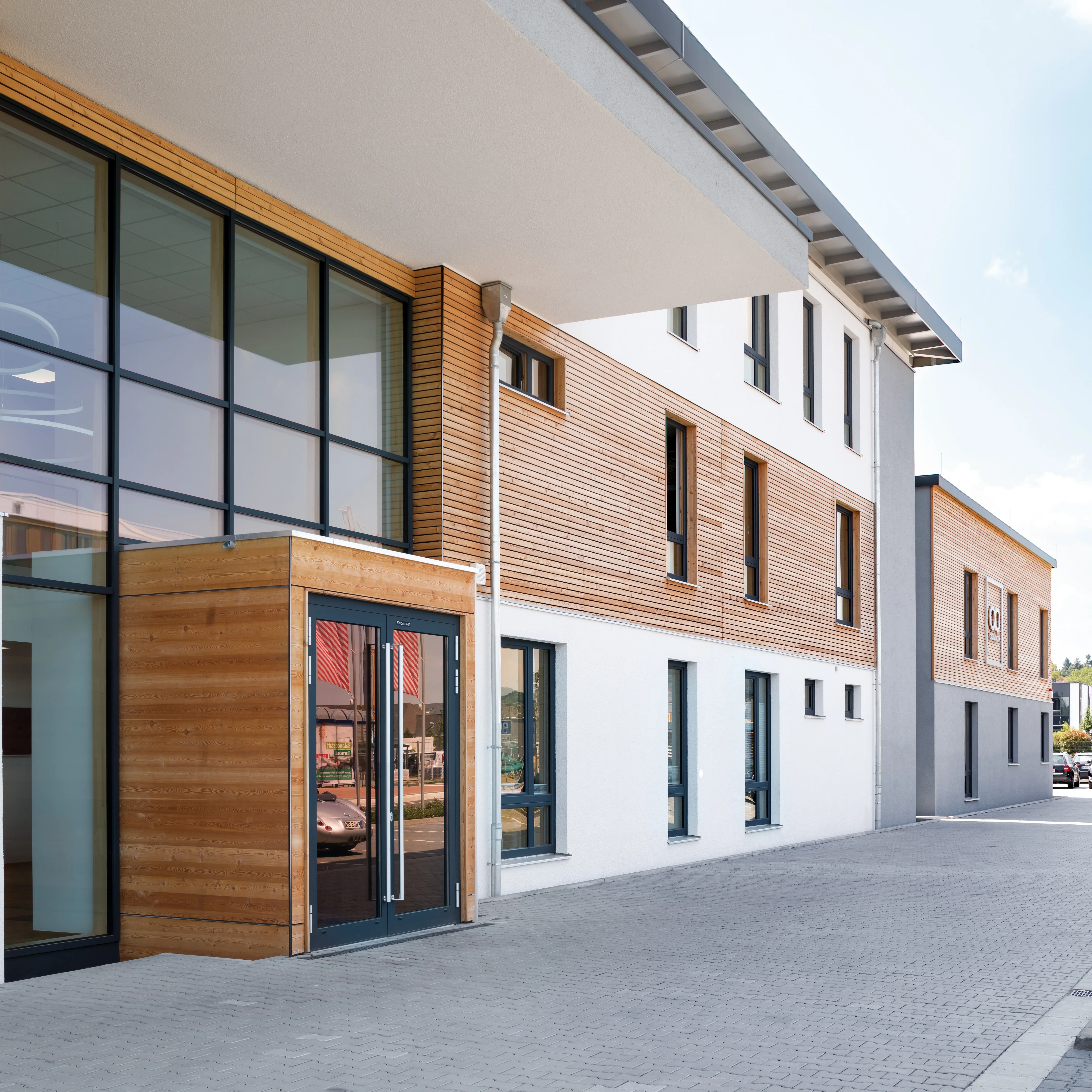 Moderne Glasfassade mit Holzverkleidung, Eingangsbereich und Fensterreihen eines Bürogebäudes.