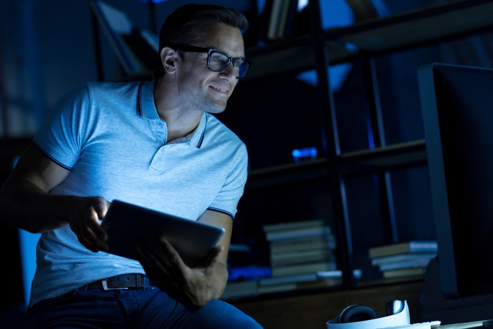 Man wearing glasses working in a dim office with a laptop, representing automated AI checks that maintain data accuracy.