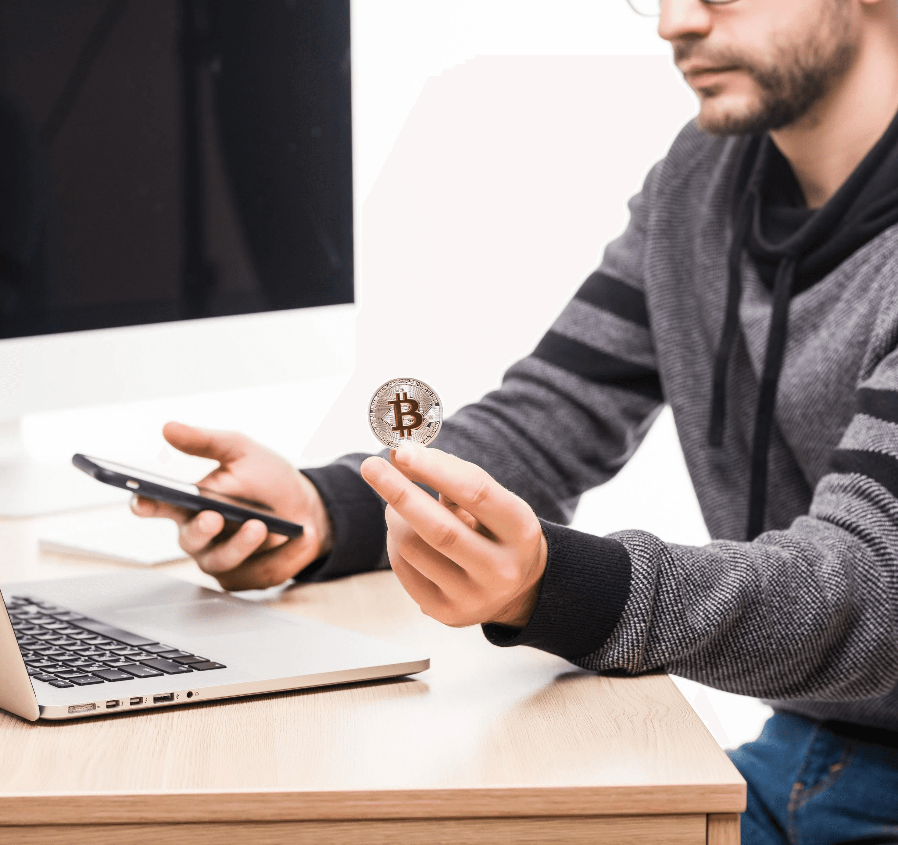 Homme tenant une pièce de Bitcoin devant son ordinateur pour investissement crypto