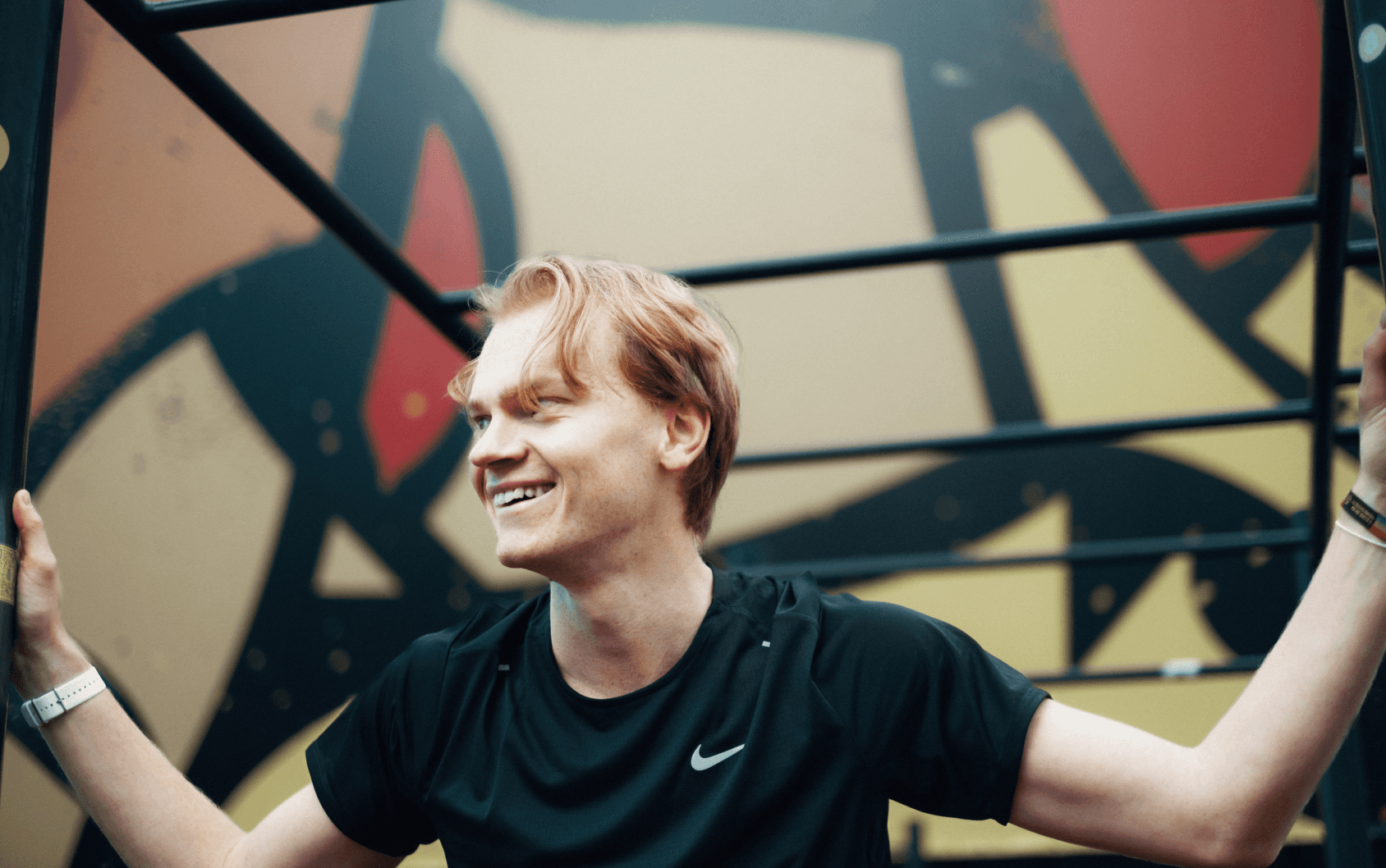 Man wearing a black Nike t shirt standing in front of a graffiti wall smiling and looking away from the camera. 