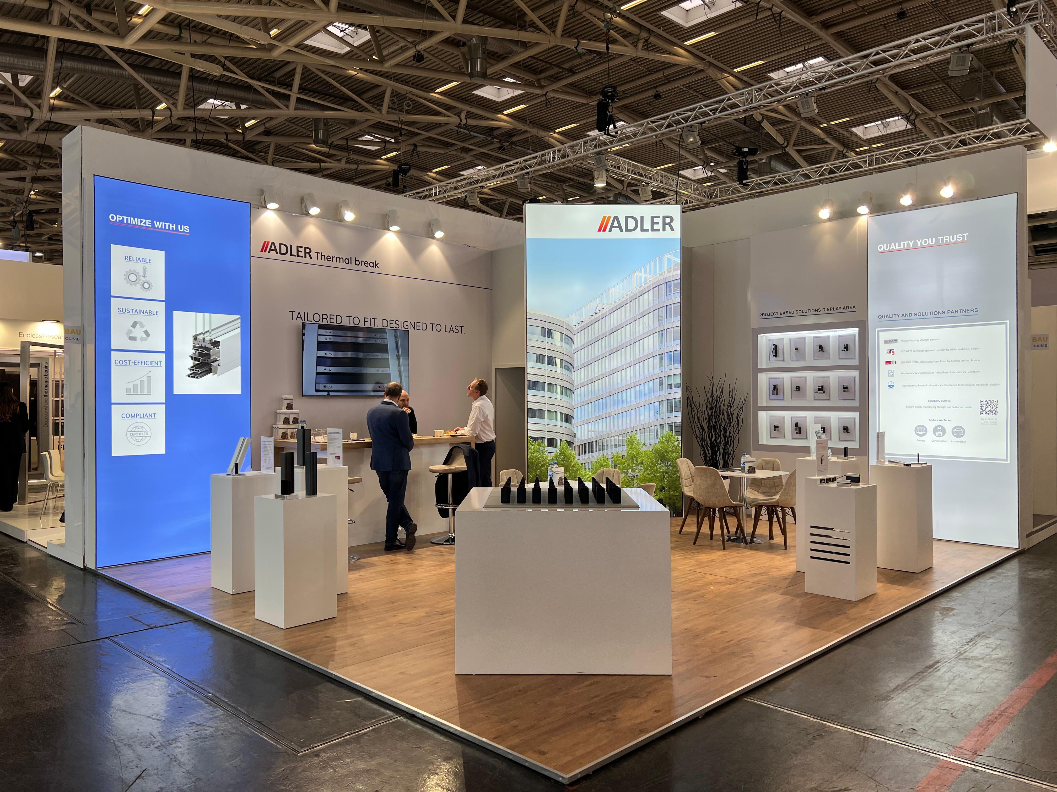 Adler exhibition stand at BAU 2025 Munich, featuring a clean, premium design with white walls, light wood flooring, and large illuminated graphics.