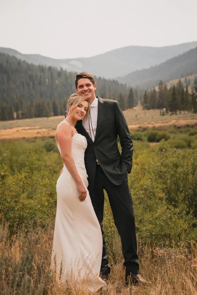 Newlyweds posing in a meadow with mountains behind them