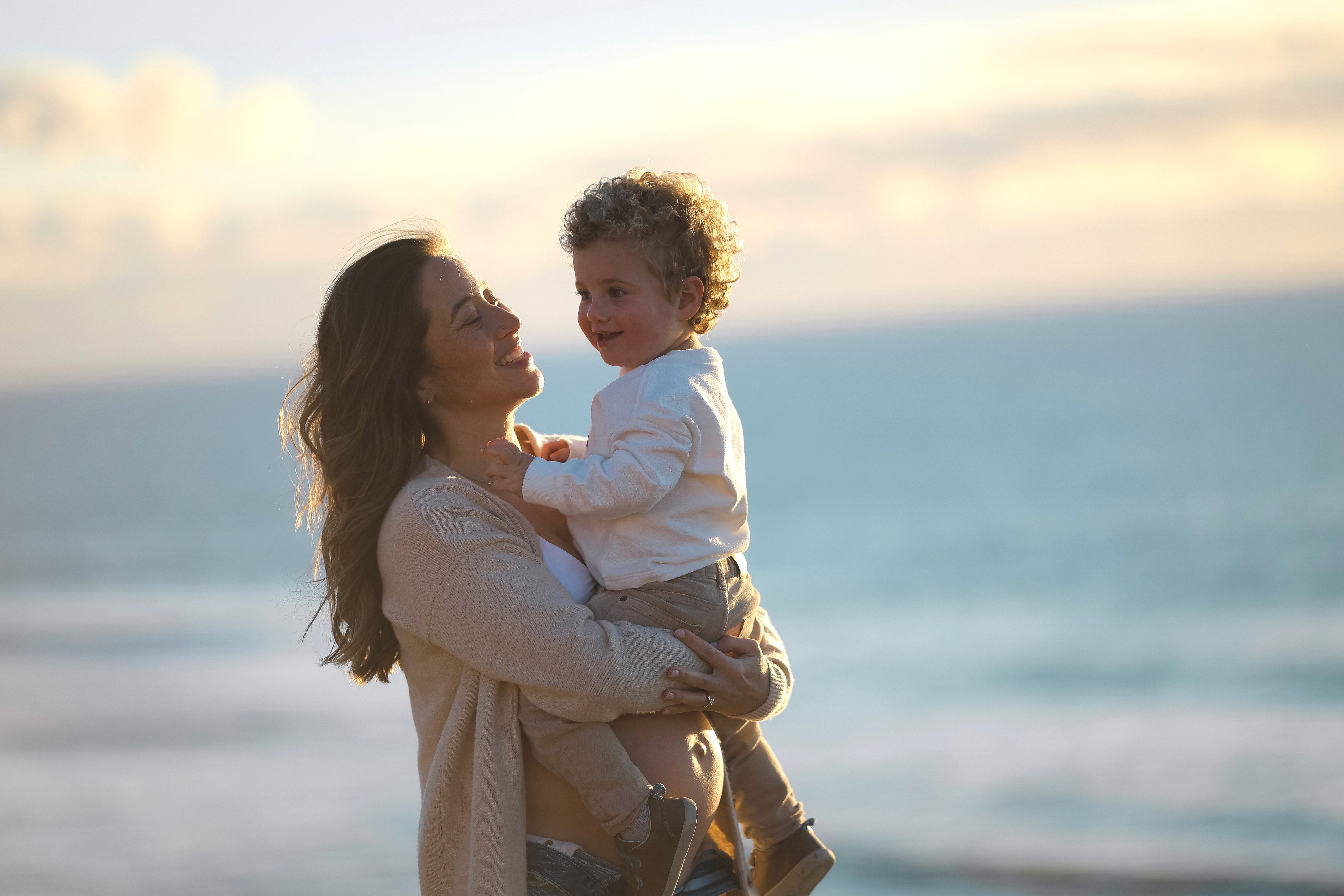 Mother lifting toddler into the air during a joyful family session at the beach.