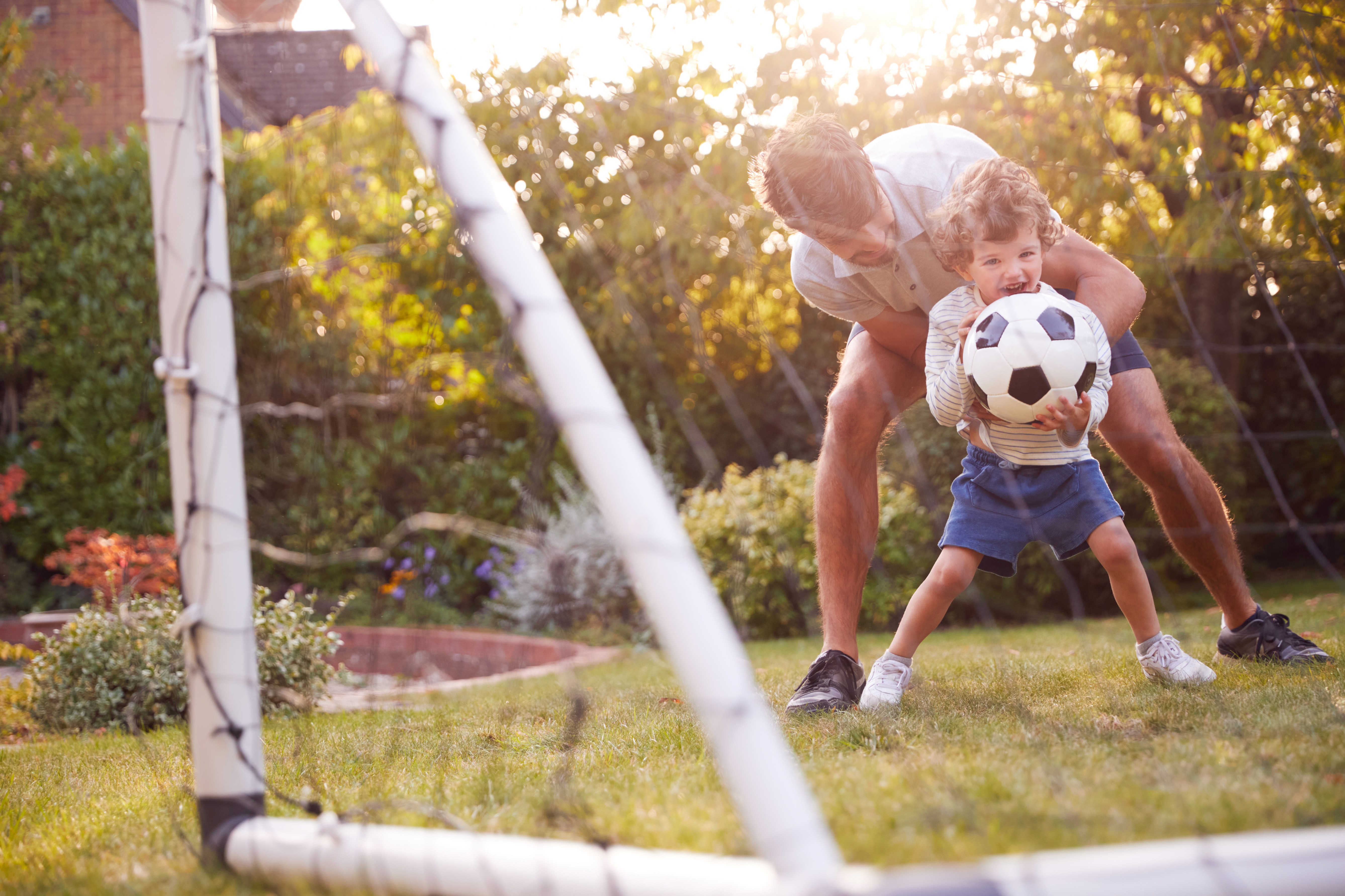 Vater spielt mit seinem Sohn im Garten Fußball und zeigt, dass bewusster Umgang mit Geld mehr Raum für gemeinsame Zeit schafft
