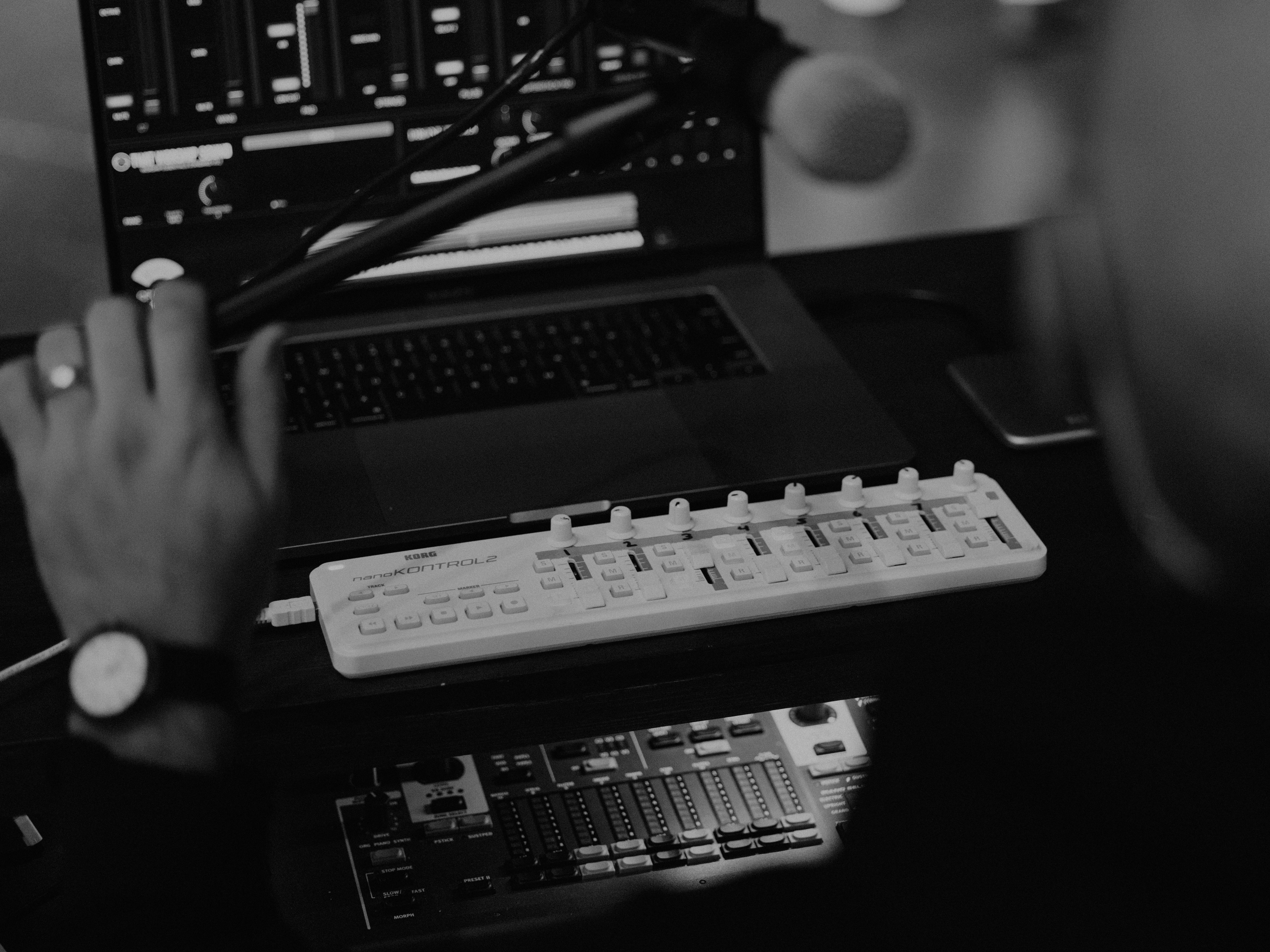 A black and white image of a producer creating music on their midi and connected DAW. Photo by Luis Morera on Unsplash