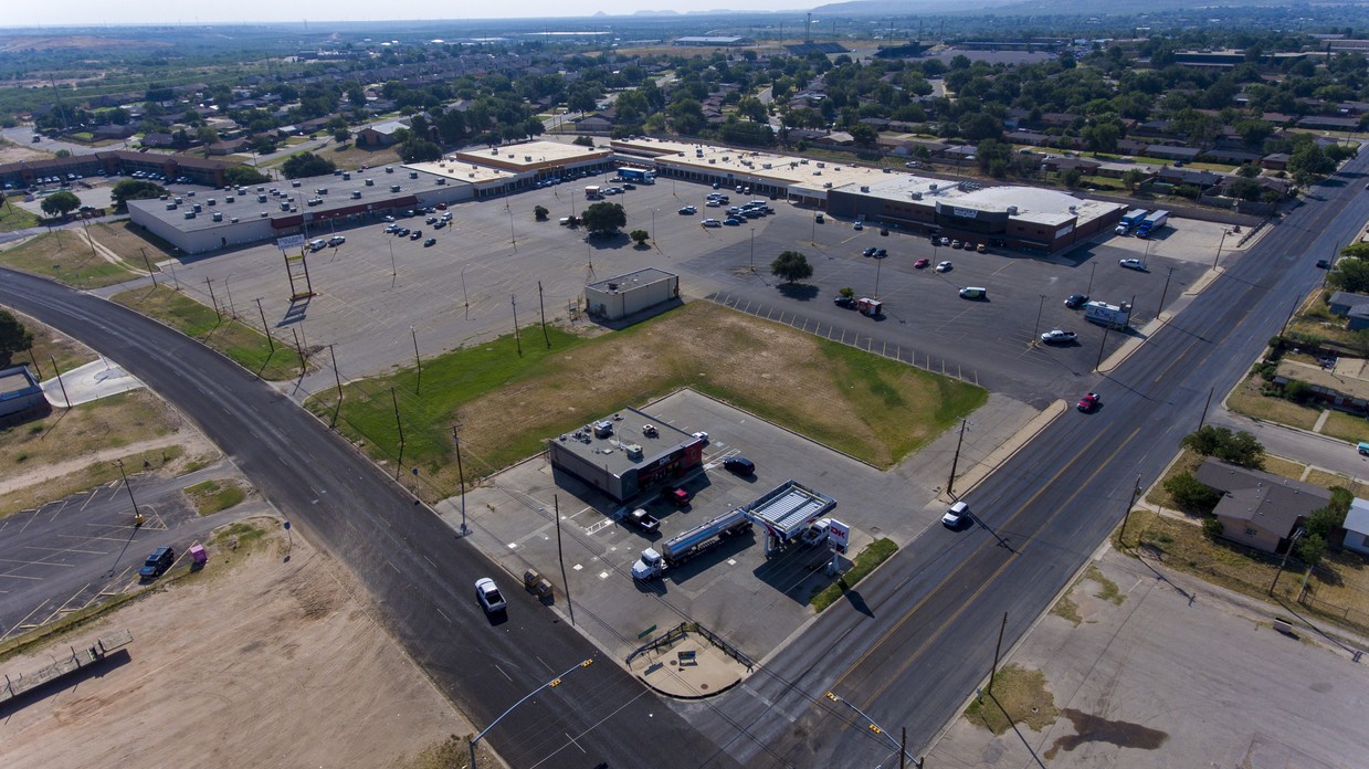 Aerial view of a large, mostly empty parking lot adjacent to a shopping center. 