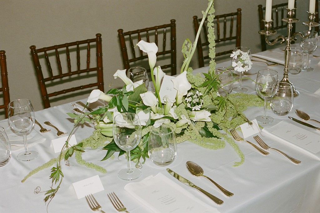 Elegant wedding table setting with white linens, calla lily floral arrangement, and candlelit reception décor
