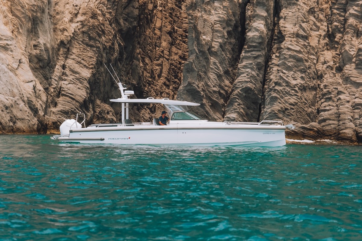 White Axopar 37 yacht anchored in crystal-clear turquoise waters beneath dramatic white limestone cliffs in the Greek islands.