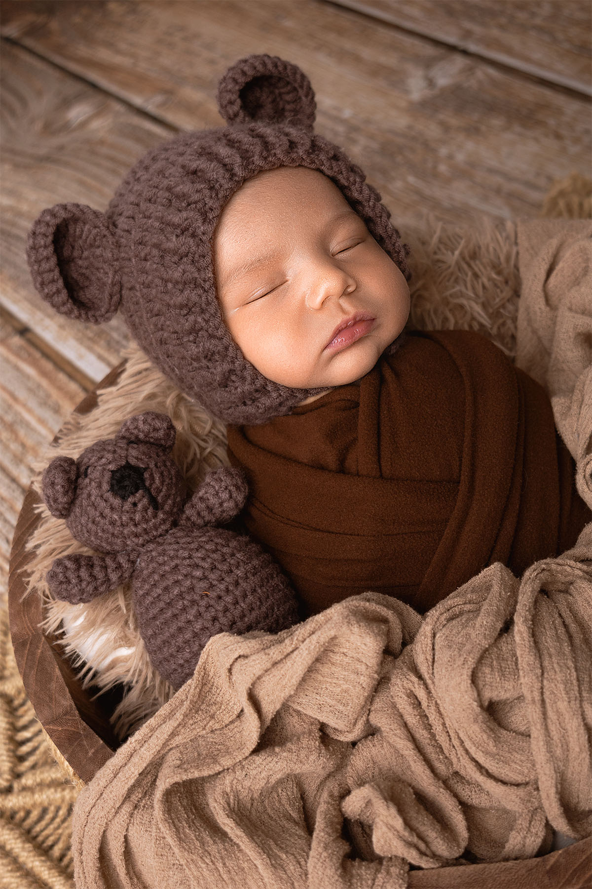 Newborn baby sleeping peacefully in a basket with plush toys.