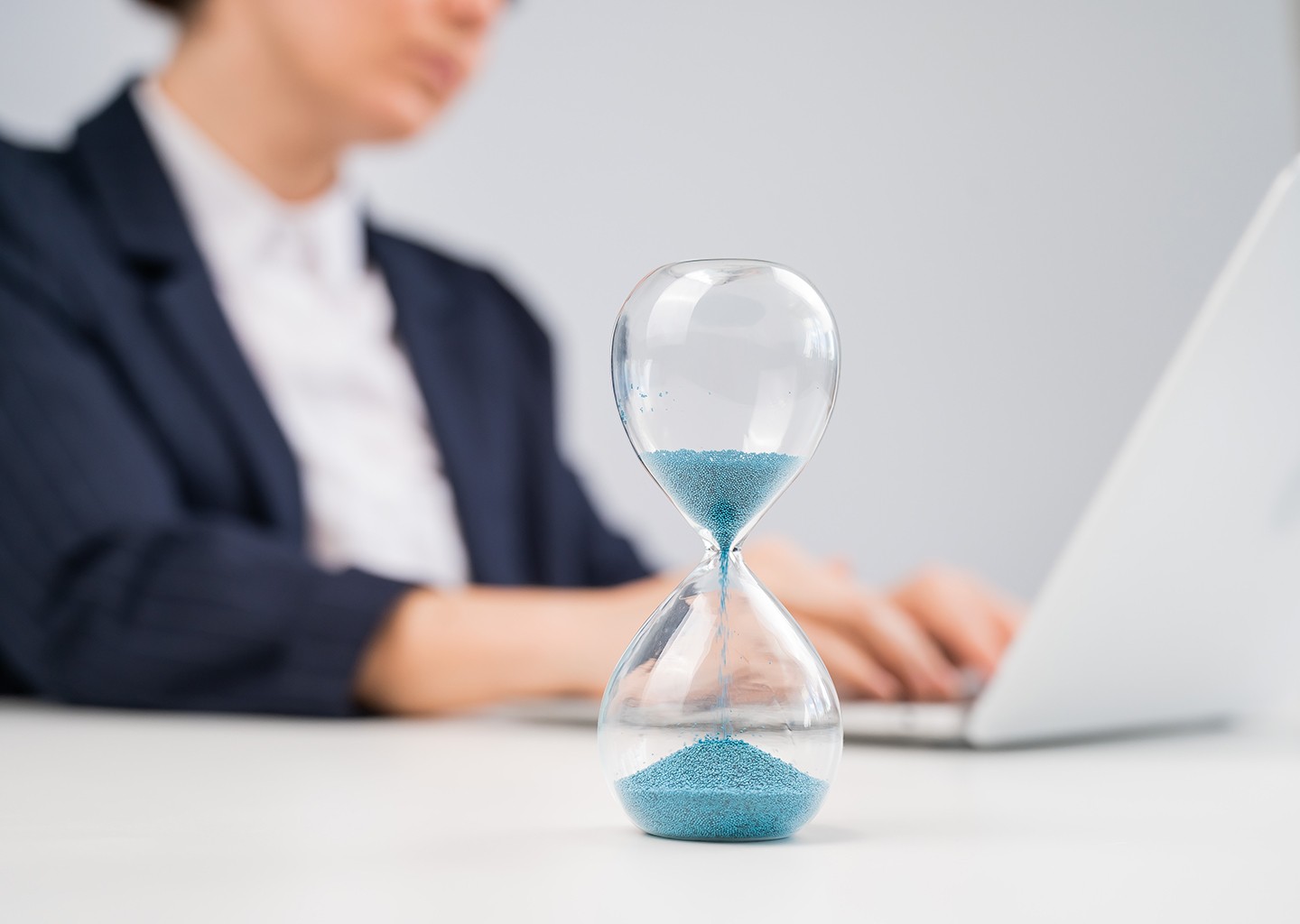 Una persona seduta alla scrivania lavora col laptop al suo time tracking software. In primo piano una clessidra simboleggia il tempo dedicato alle attività