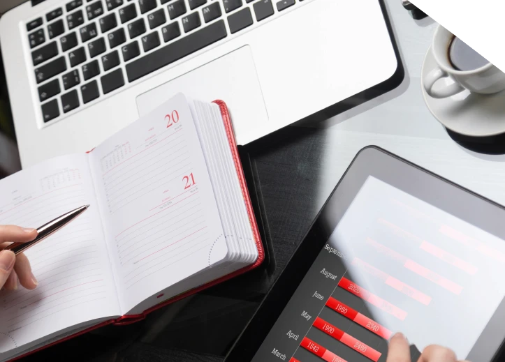 Close-up of hands making notes in diary next to tablet computer