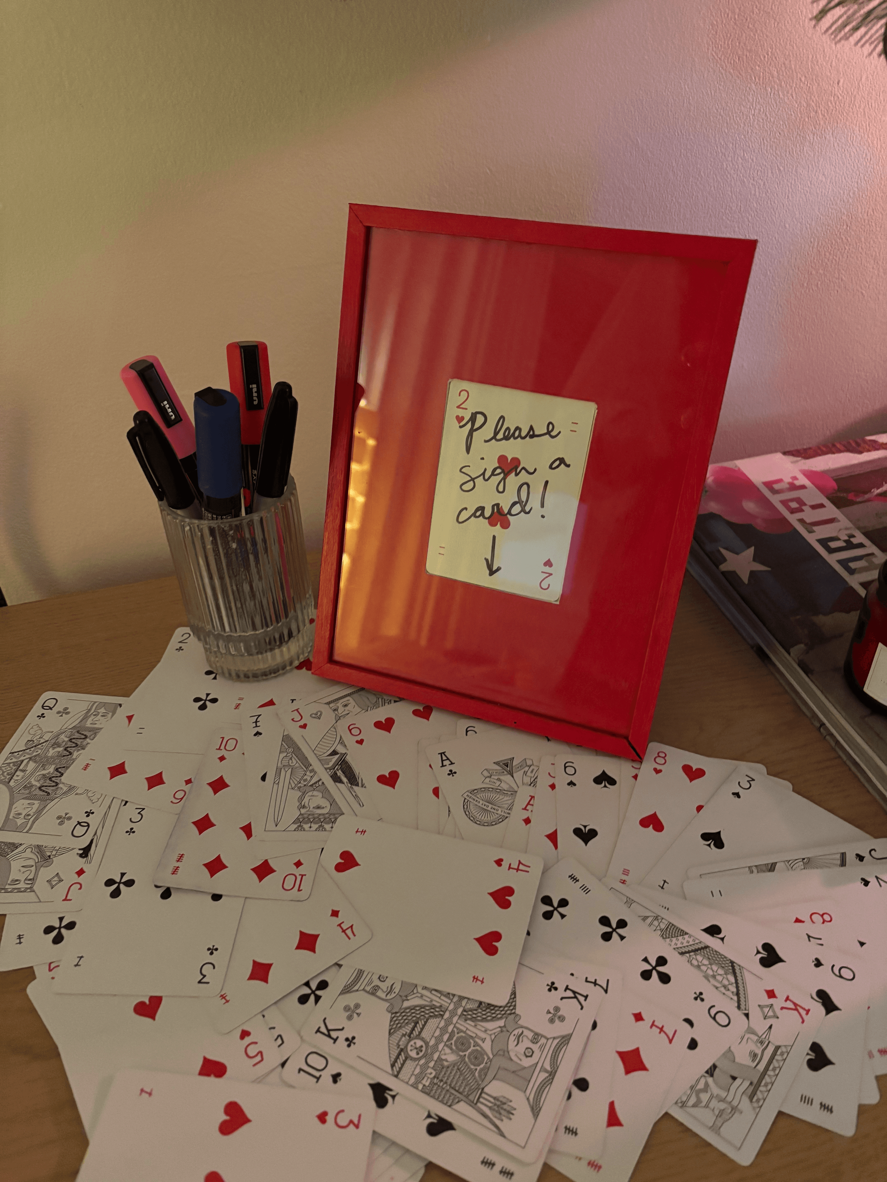 A tabletop with a red binder, scattered playing cards, and a pen holder in the background.