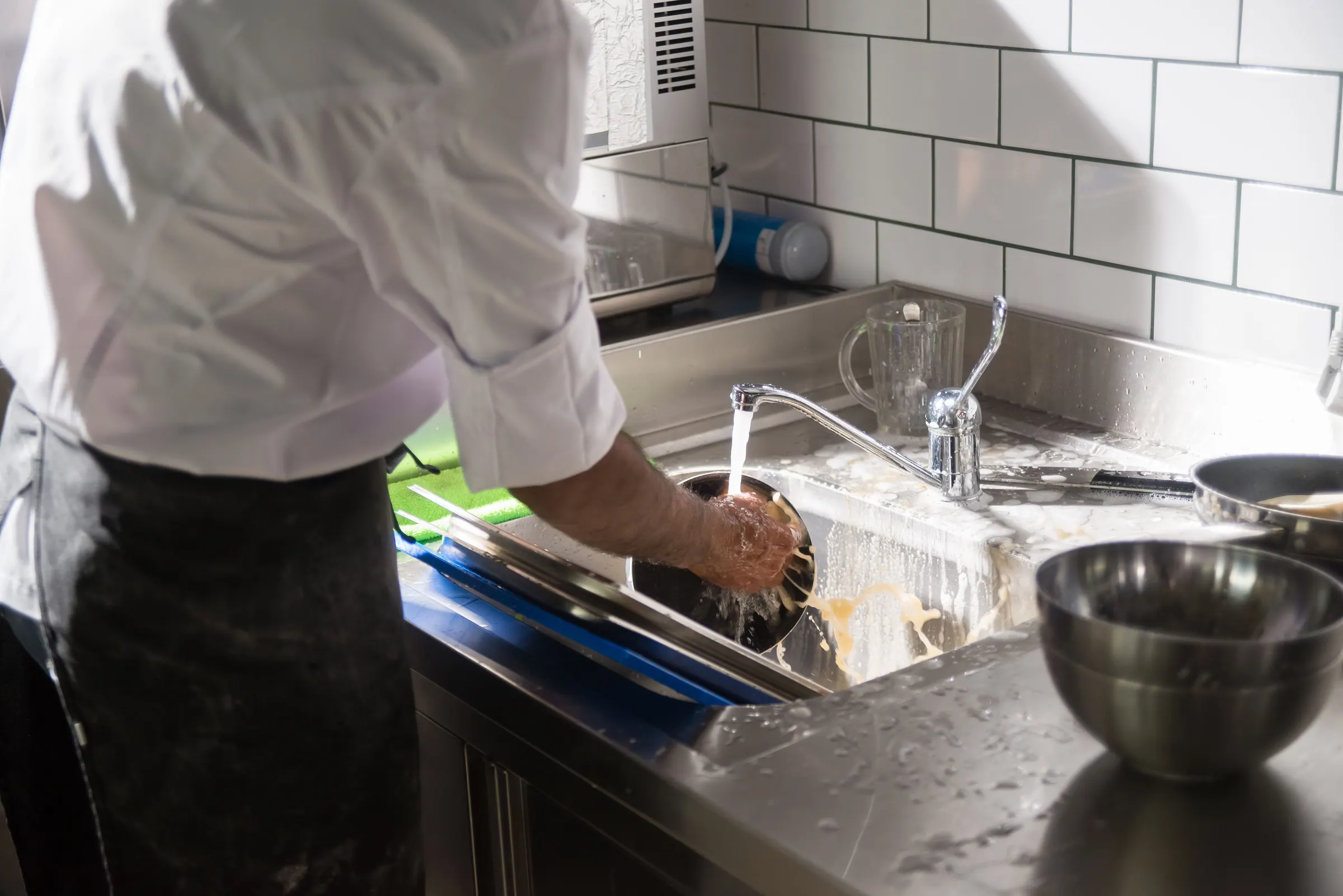 Chef washing dishes at a stainless steel commercial kitchen sink