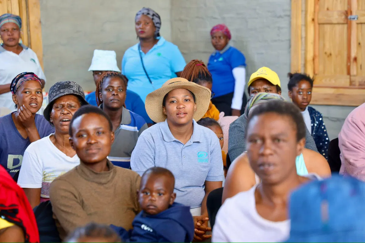 A young woman with long hair smiles while standing against a green backdrop, wearing a casual dark sweater.