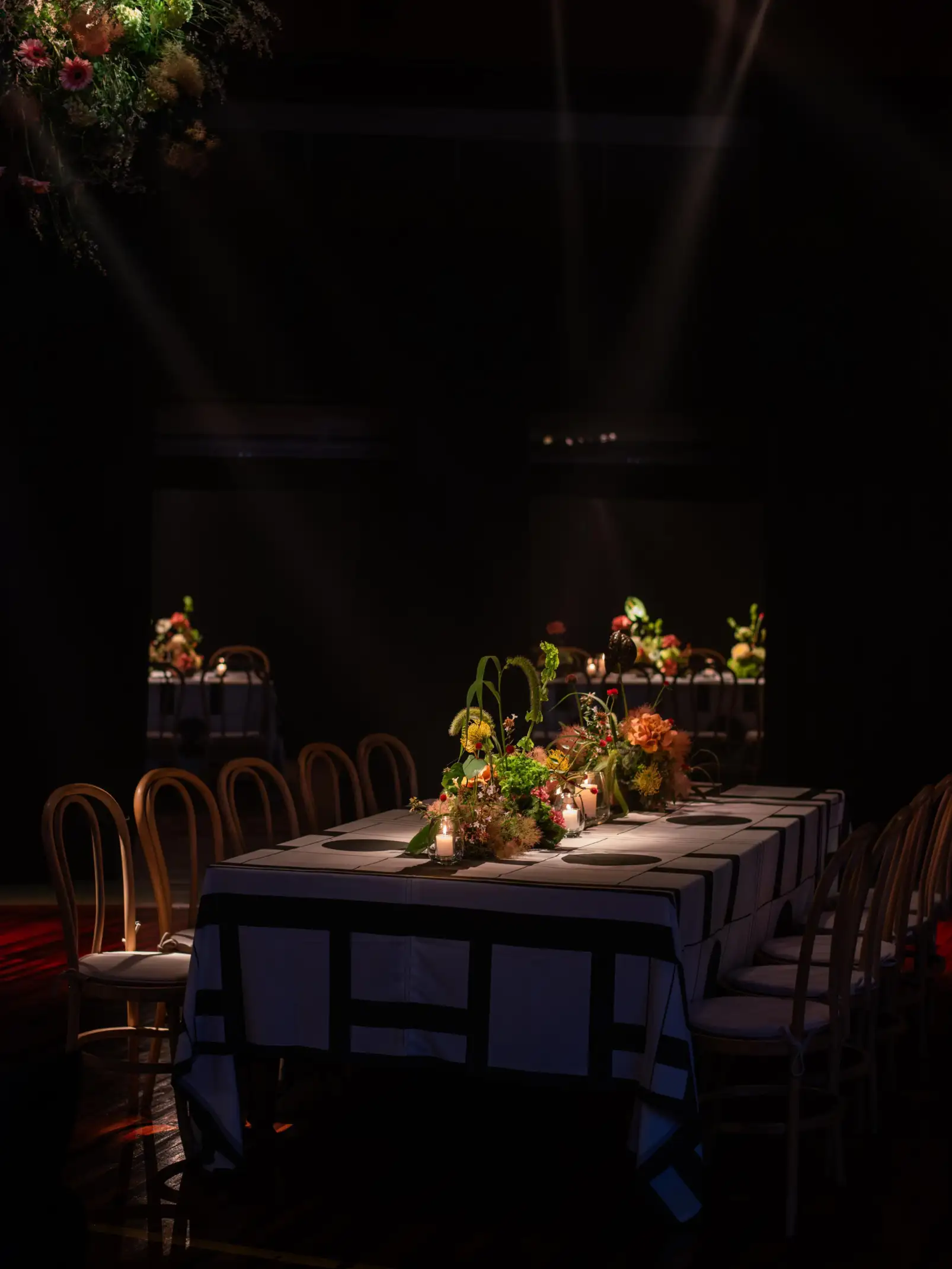 Mesa de evento iluminada por focos de luz, con centros florales naturales y velas encendidas en tonos cálidos.