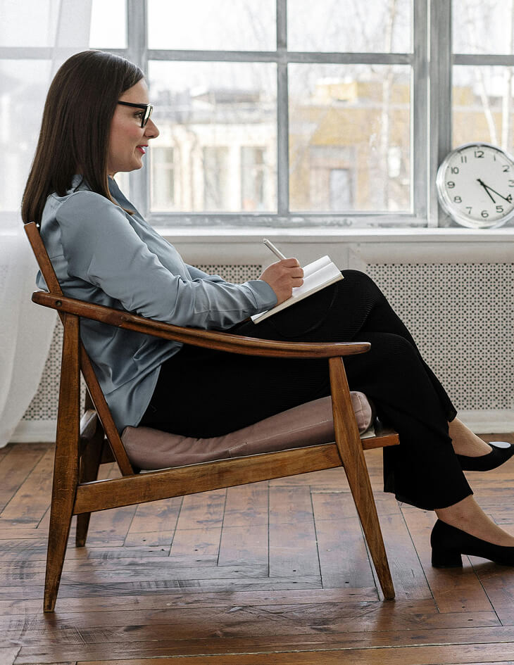 Therapist sitting in a chair and writing in a notebook during a session