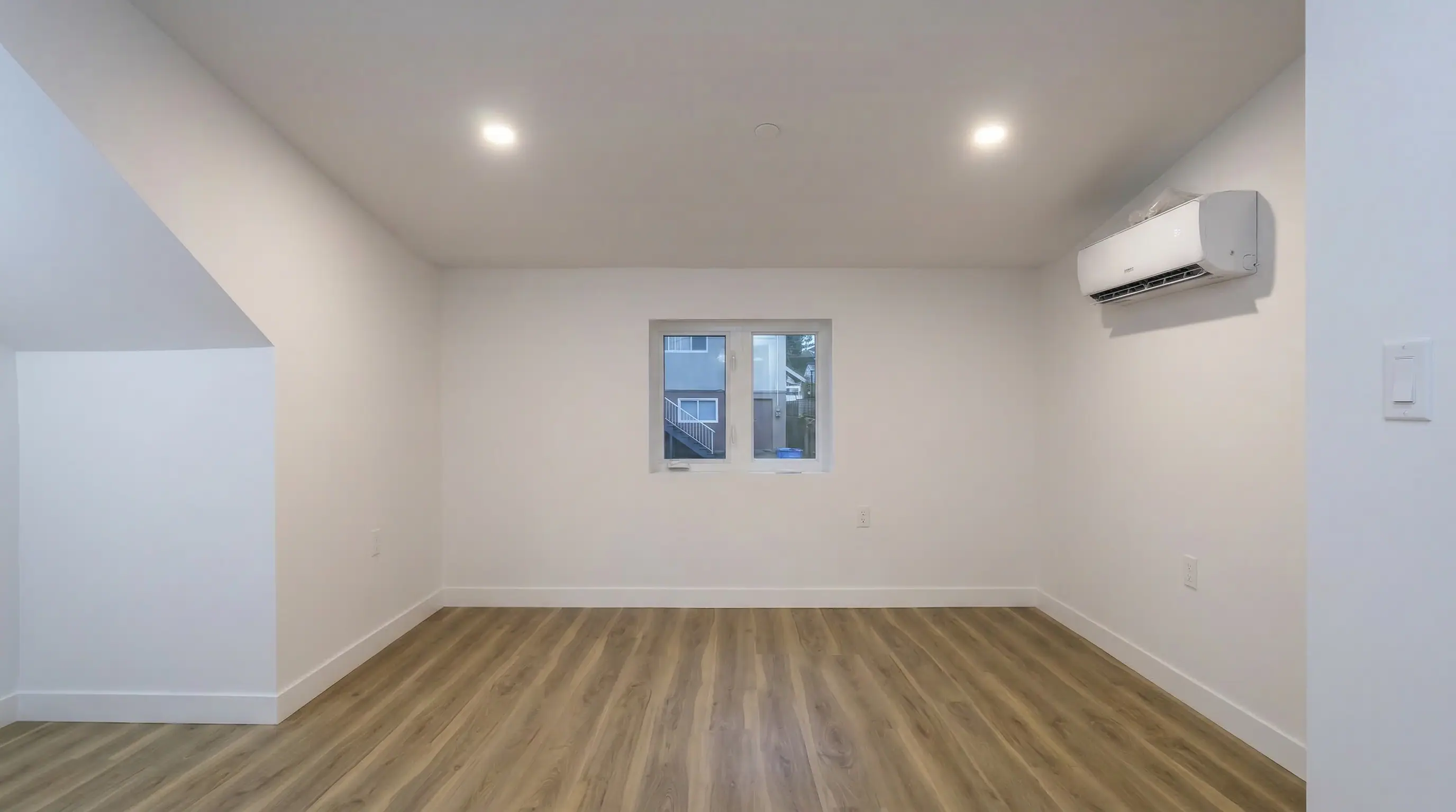 Open upper-floor bedroom loft in Vancouver Custom Homes' East 63rd laneway house, featuring hardwood-style flooring, recessed lighting, and a wall-mounted ductless heat pump.