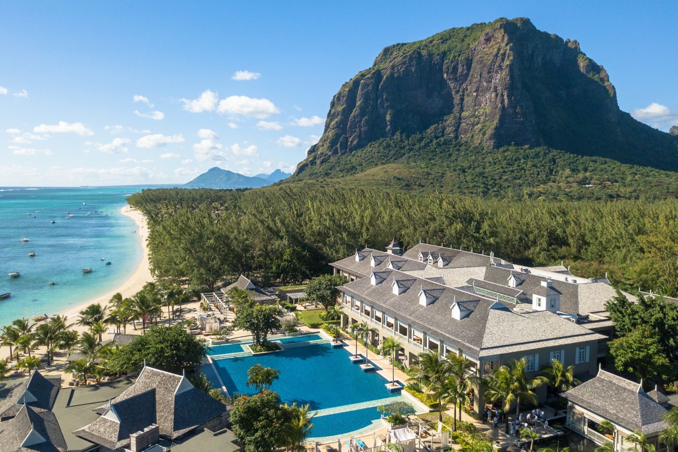 Blick aus der Vogelperspektive auf die großzügige Poolanlage und das Hauptgebäude eines Resorts auf Mauritius, umgeben von Palmen und mit dem markanten Le Morne Berg im Hintergrund.