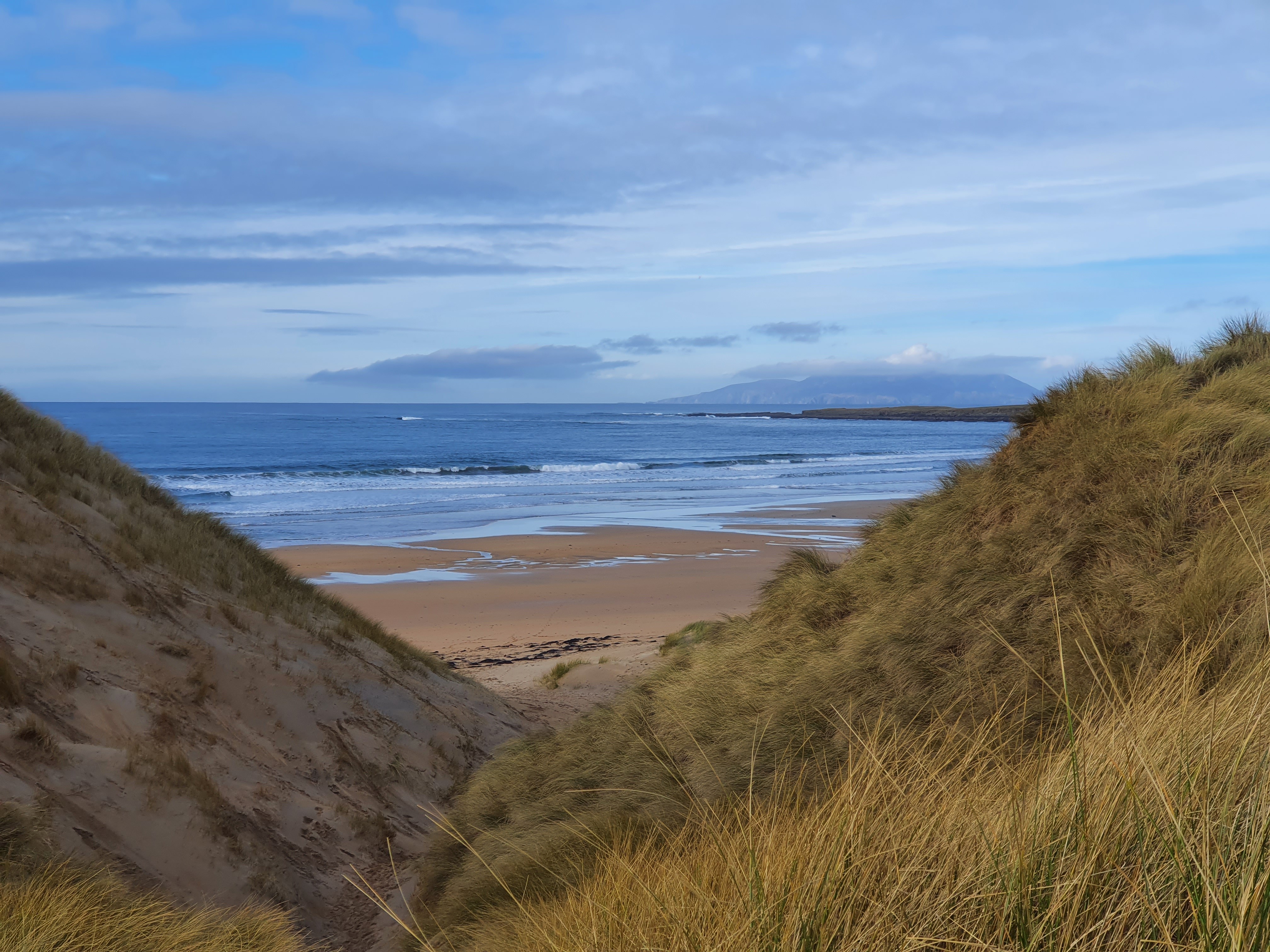 A scenic view of a valley surrounded by hills under a blue sky with fluffy clouds.