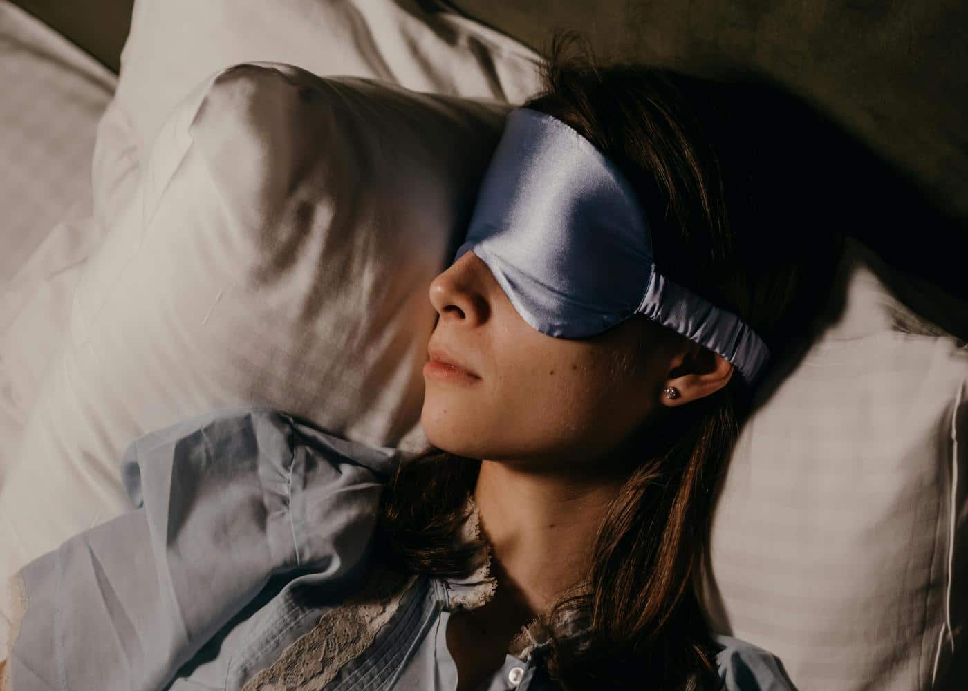 Woman laying on pillow with a blue eye mask on