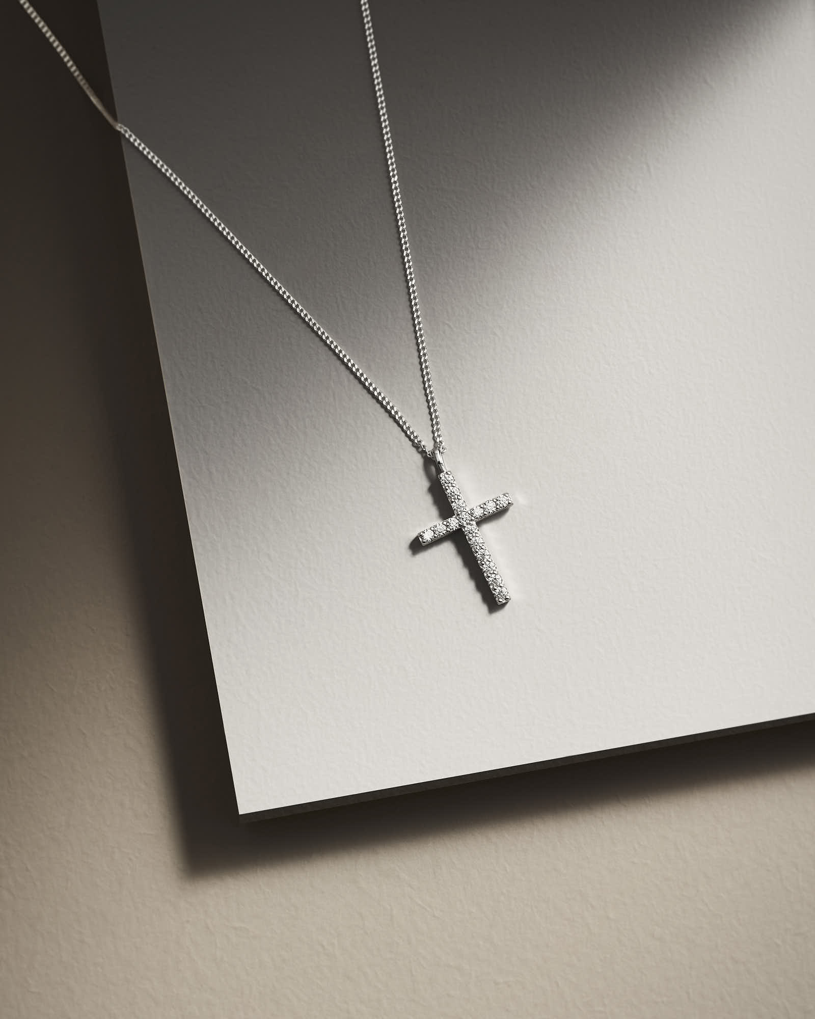 A close-up of a silver cross necklace resting on a reflective surface.