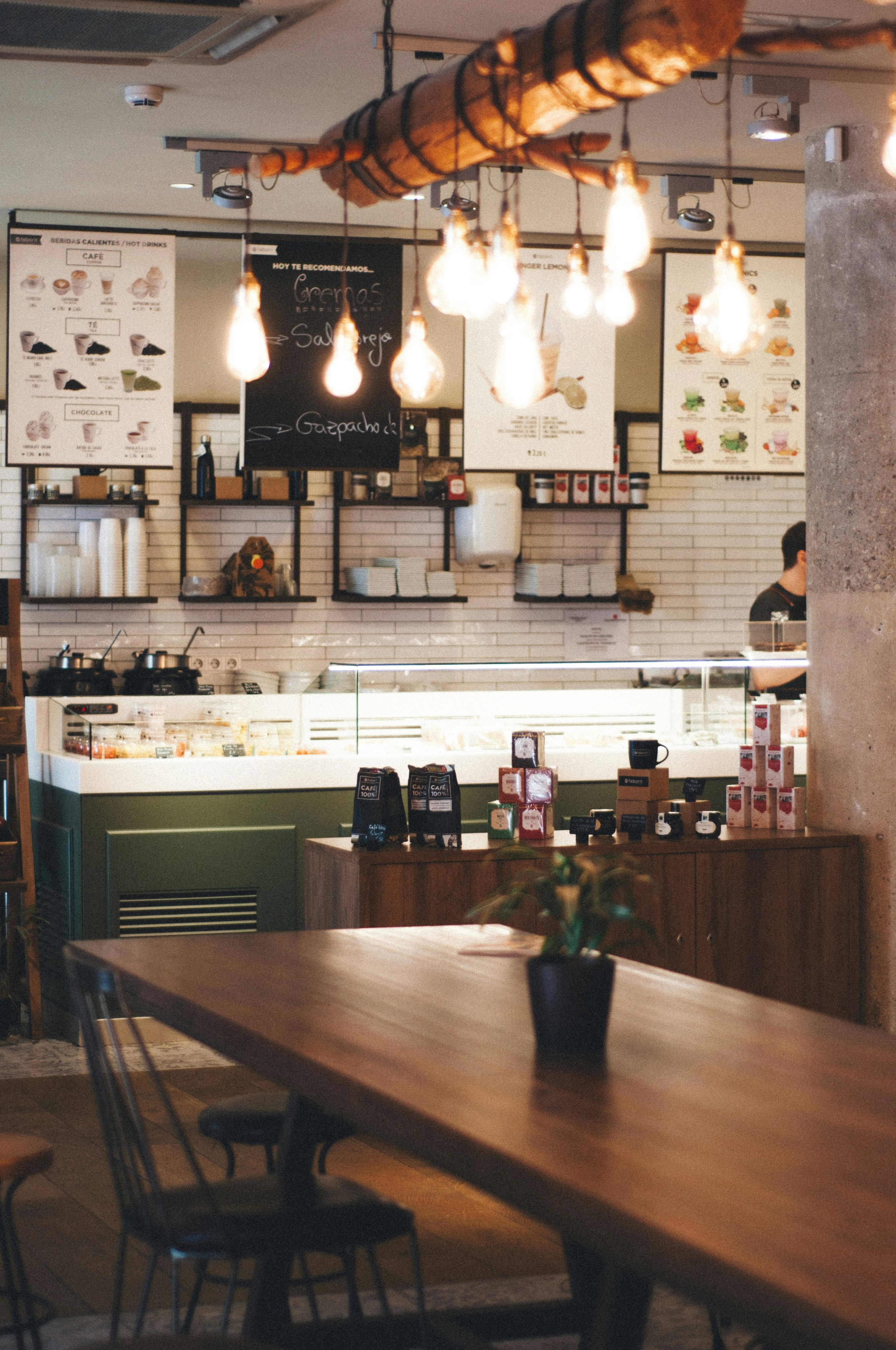 Cozy cafe interior featuring wooden furniture, pendant lights, and a well-organized counter with plants.
