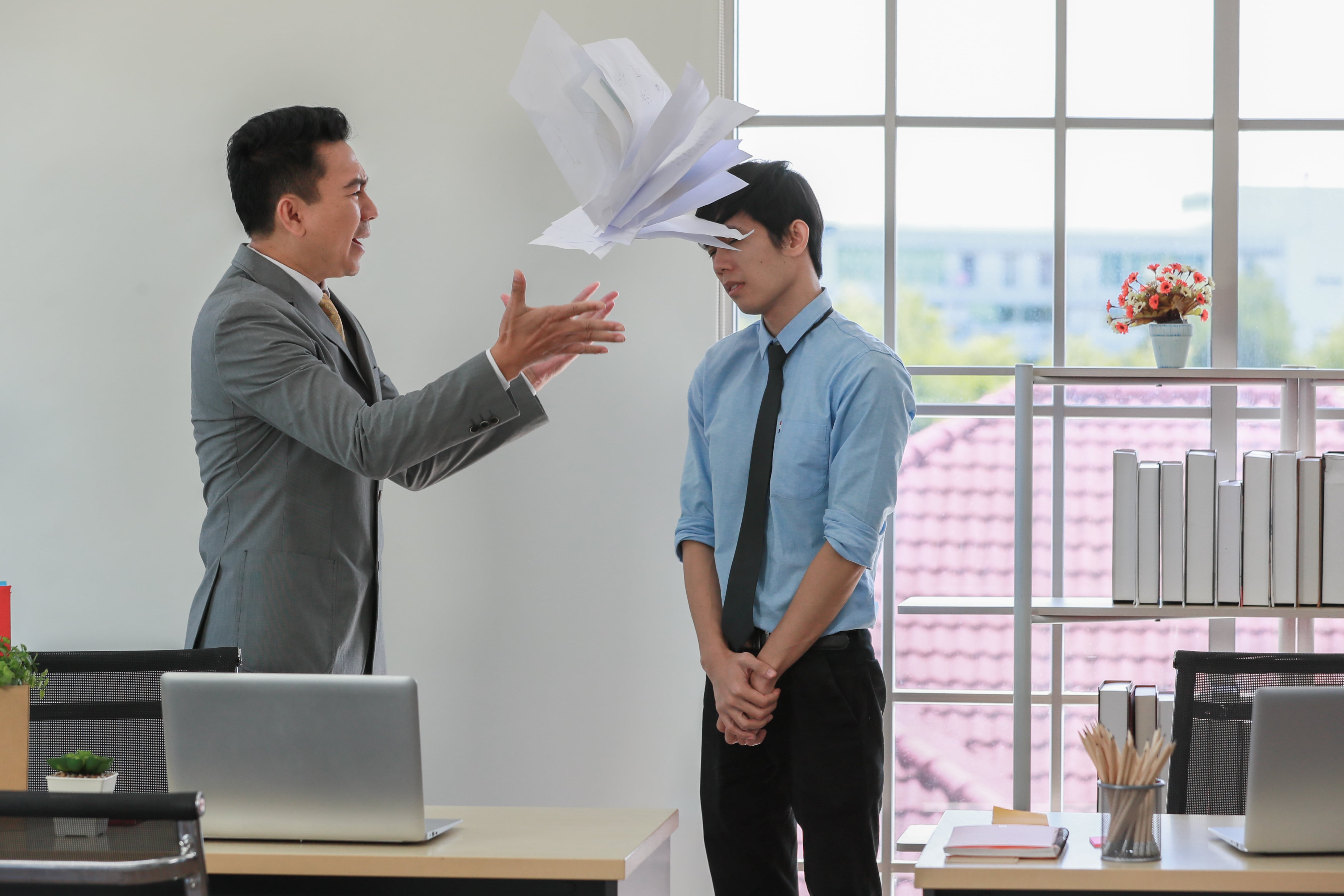 A man throwing papers in the air in anger in front of another man 