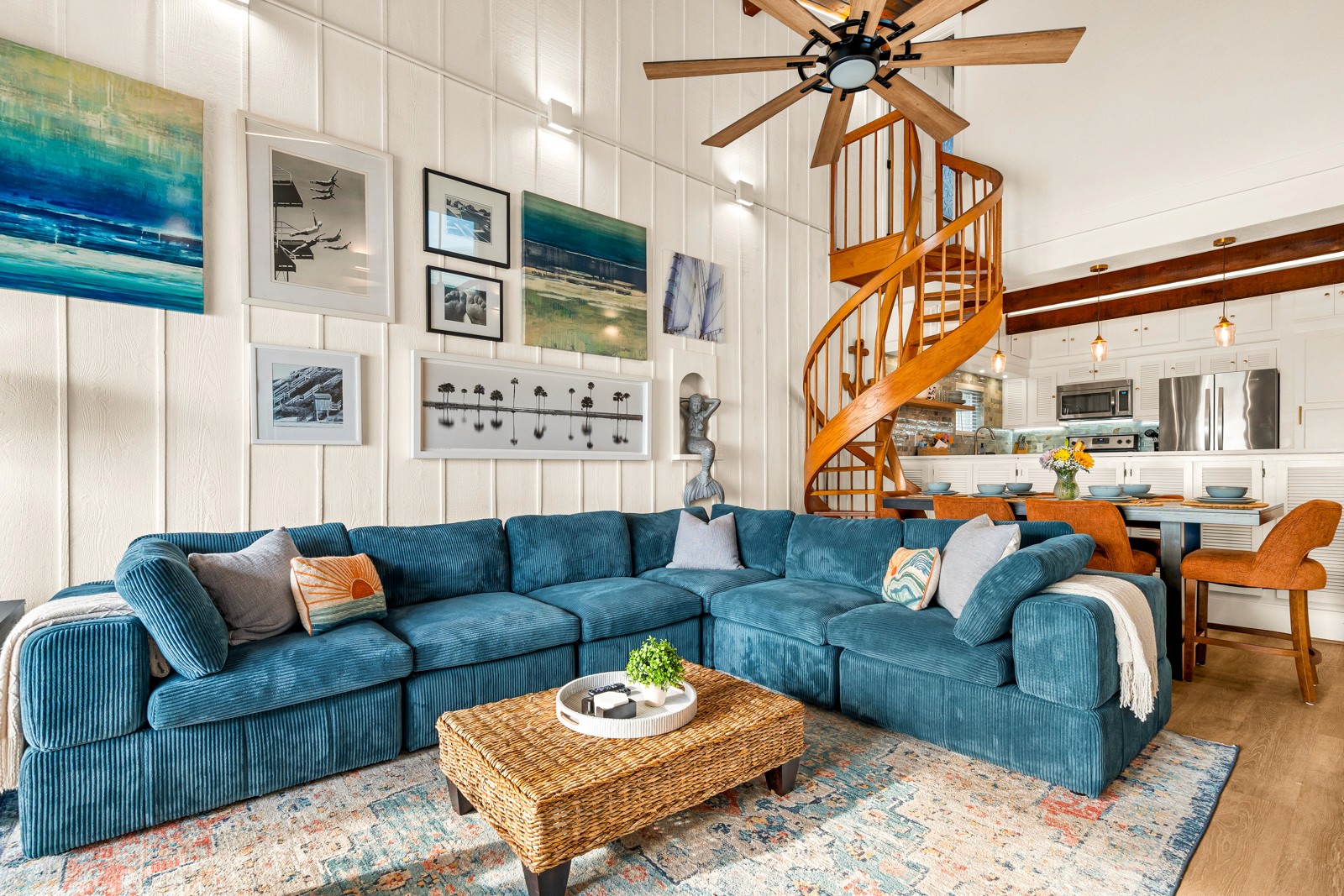 Indian Shores Airbnb living room with a teal sectional sofa, coastal wall art, vaulted ceilings, spiral staircase and open kitchen
