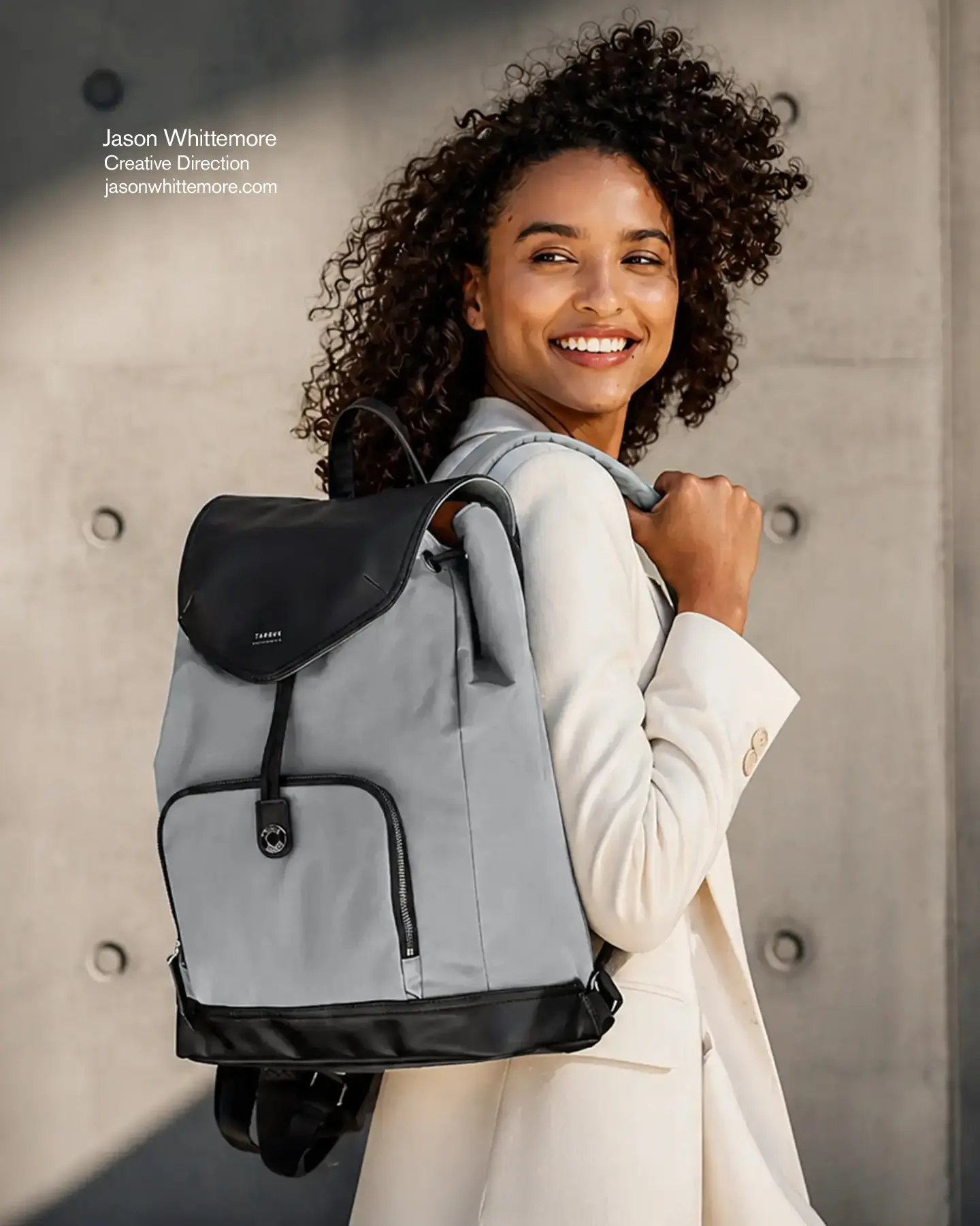 Woman wearing a gray Newport backpack against a concrete architectural backdrop.