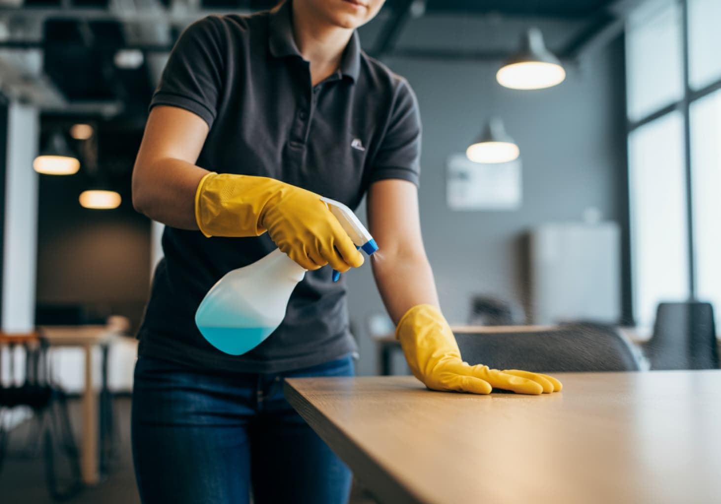 Woman holding a spray bottle cleaning a wood table in a breakroom