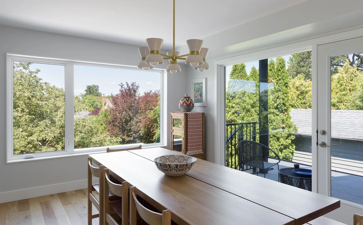 Modern two-story home with large glass windows, warmly lit interiors, and a balcony. Surrounded by trees and a manicured lawn at dusk. Cozy ambiance.