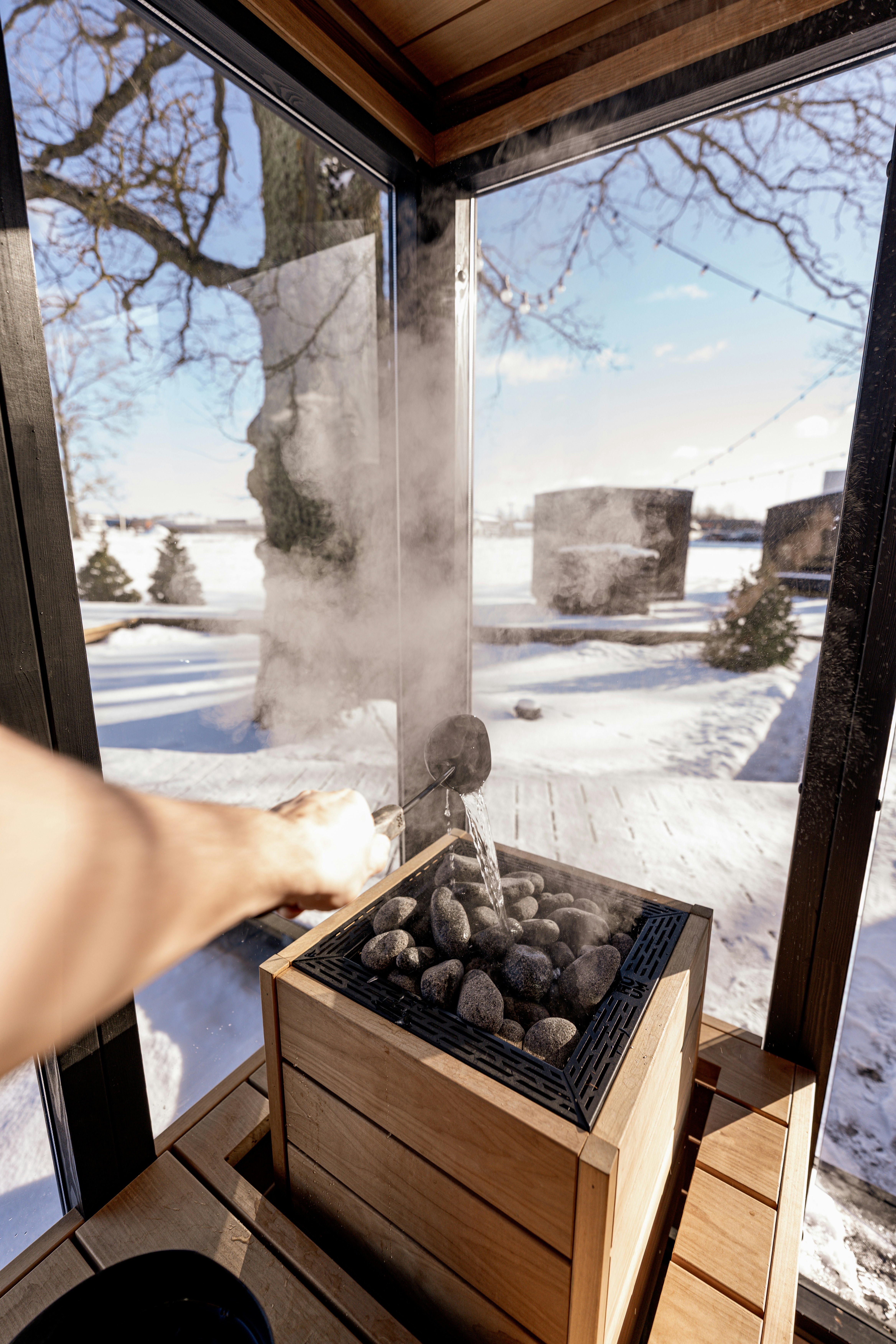 Man pours water on sauna rocks, creating steam.