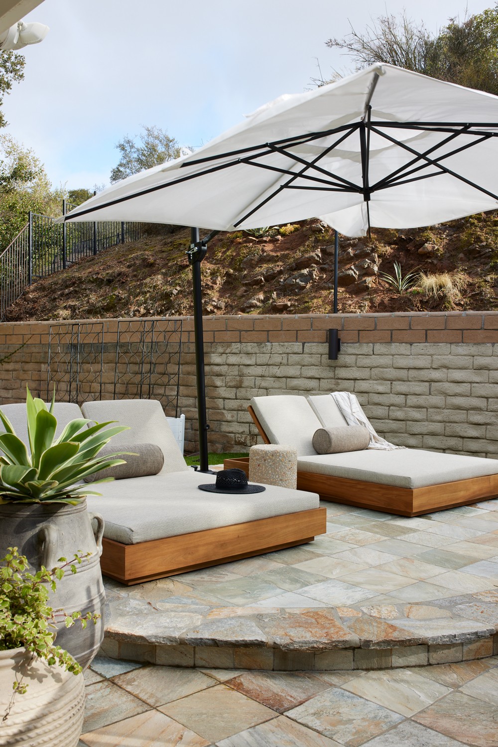 Luxurious poolside loungers, a grand umbrella, and natural slate tiles create an elegant focal point in the backyard