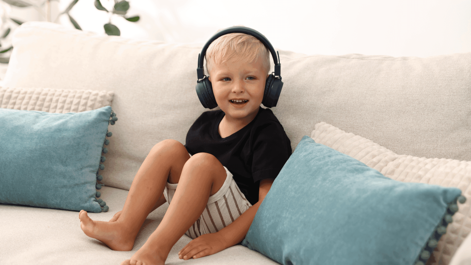A child sitting on a sofa, wearing headphones and smiling while listening to HushAway®’s Sound Sanctuary.
