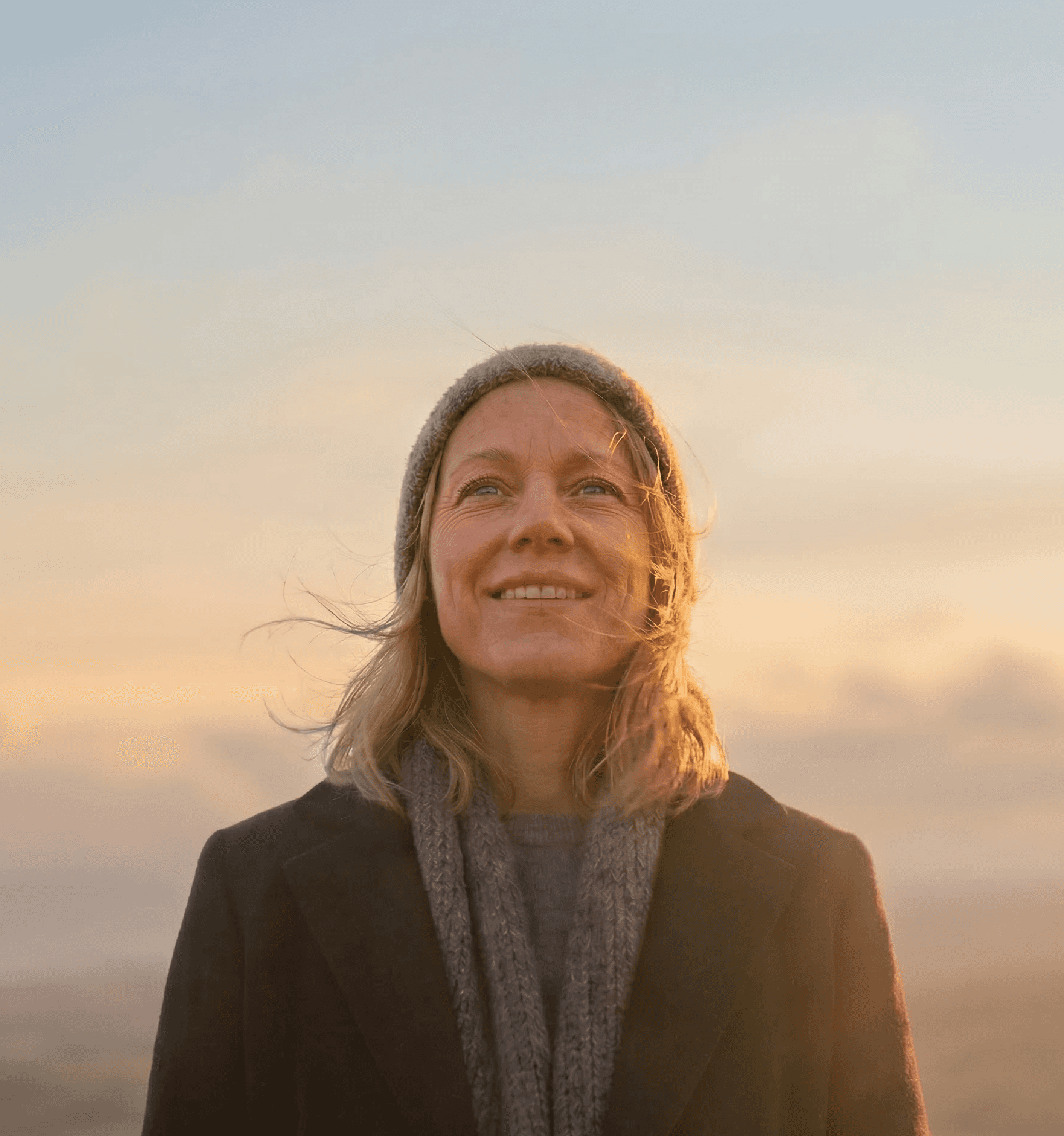 Vrouw kijkt hoopvol naar de horizon in warm zonlicht