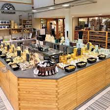 Gourmet cheese counter displaying extensive selection of artisanal cheeses on wooden deli counter in specialty food shop