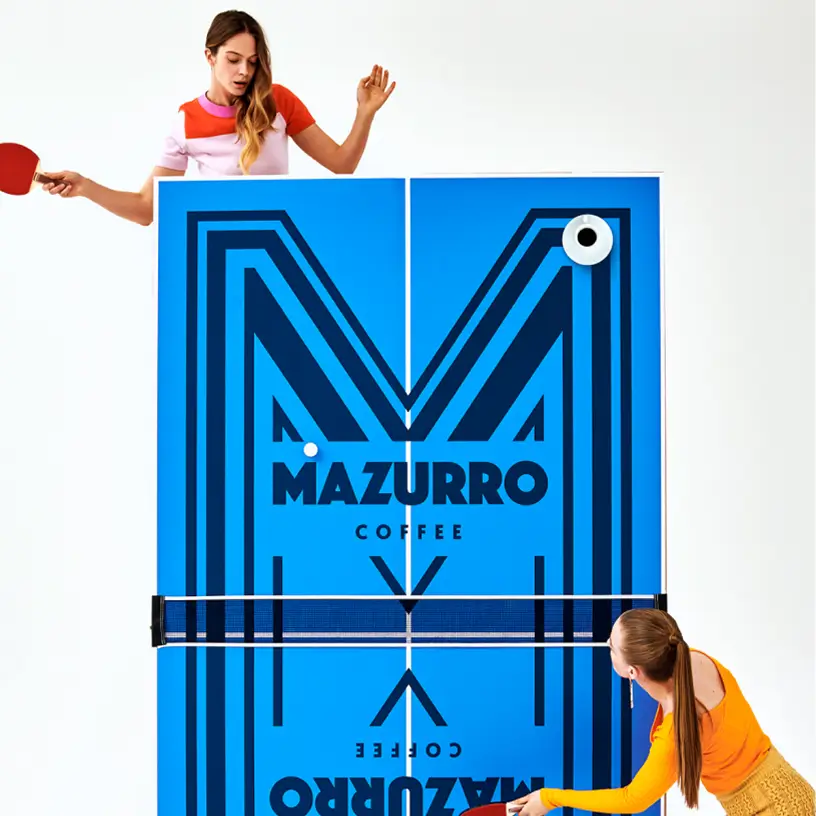 Dwie osoby grające w ping-ponga przy dużym logo Mazurro Coffee